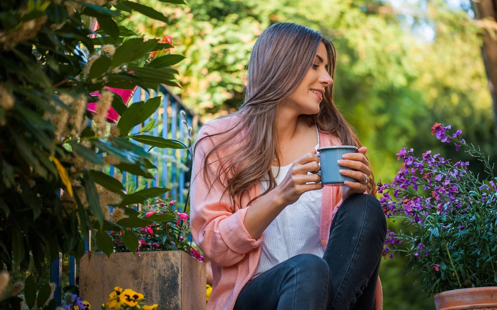 Junge Frau sitzt im Garten und schaut auf ihre Pflanzen. Sie trinkt eine zubereitete Zichorienwurzel als Kaffee-Ersatz.