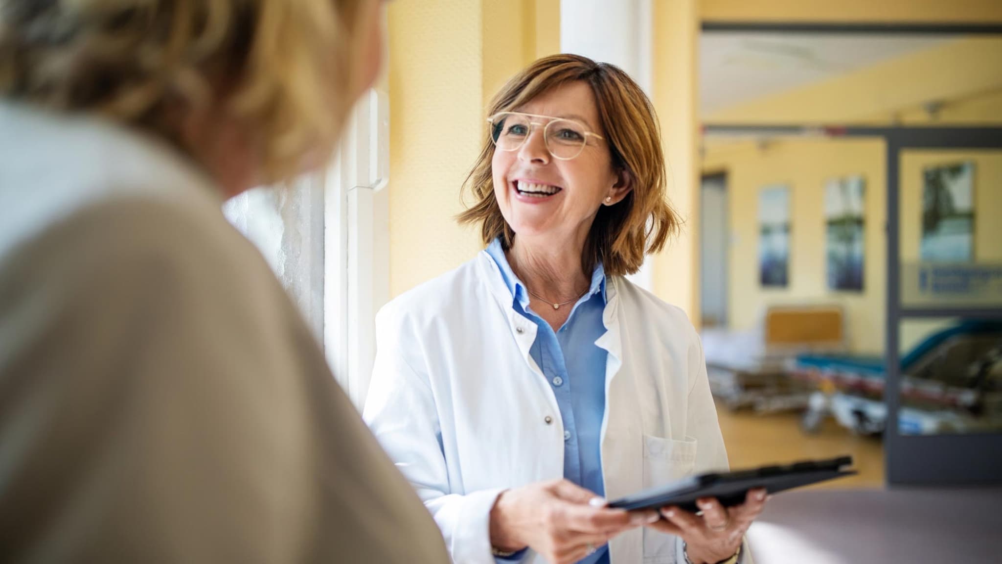DMP: Ärztin mit Brille und Klemmbrett lächelt ihre Patientin an.