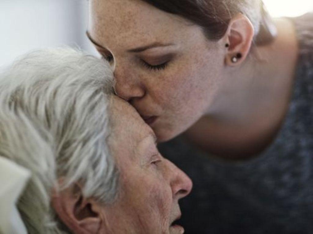 pflegebedürftig: Tochter küsst ihre pflegebedürftige Mutter auf die Stirn