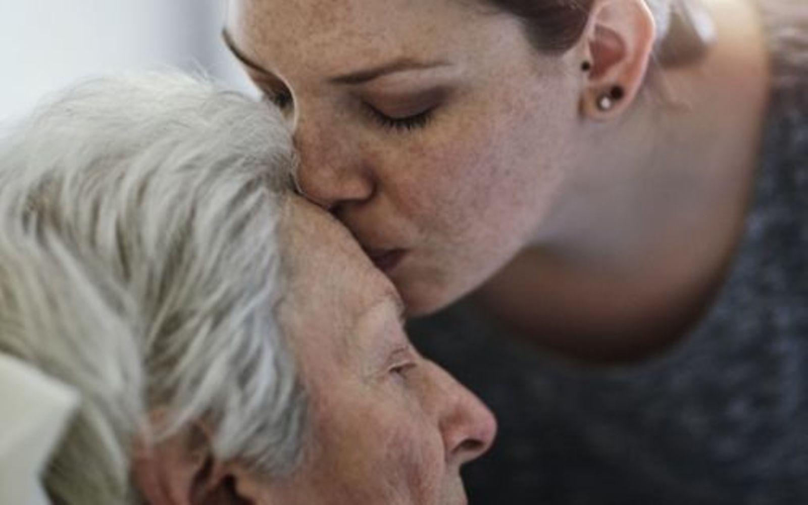 pflegebedürftig: Tochter küsst ihre pflegebedürftige Mutter auf die Stirn