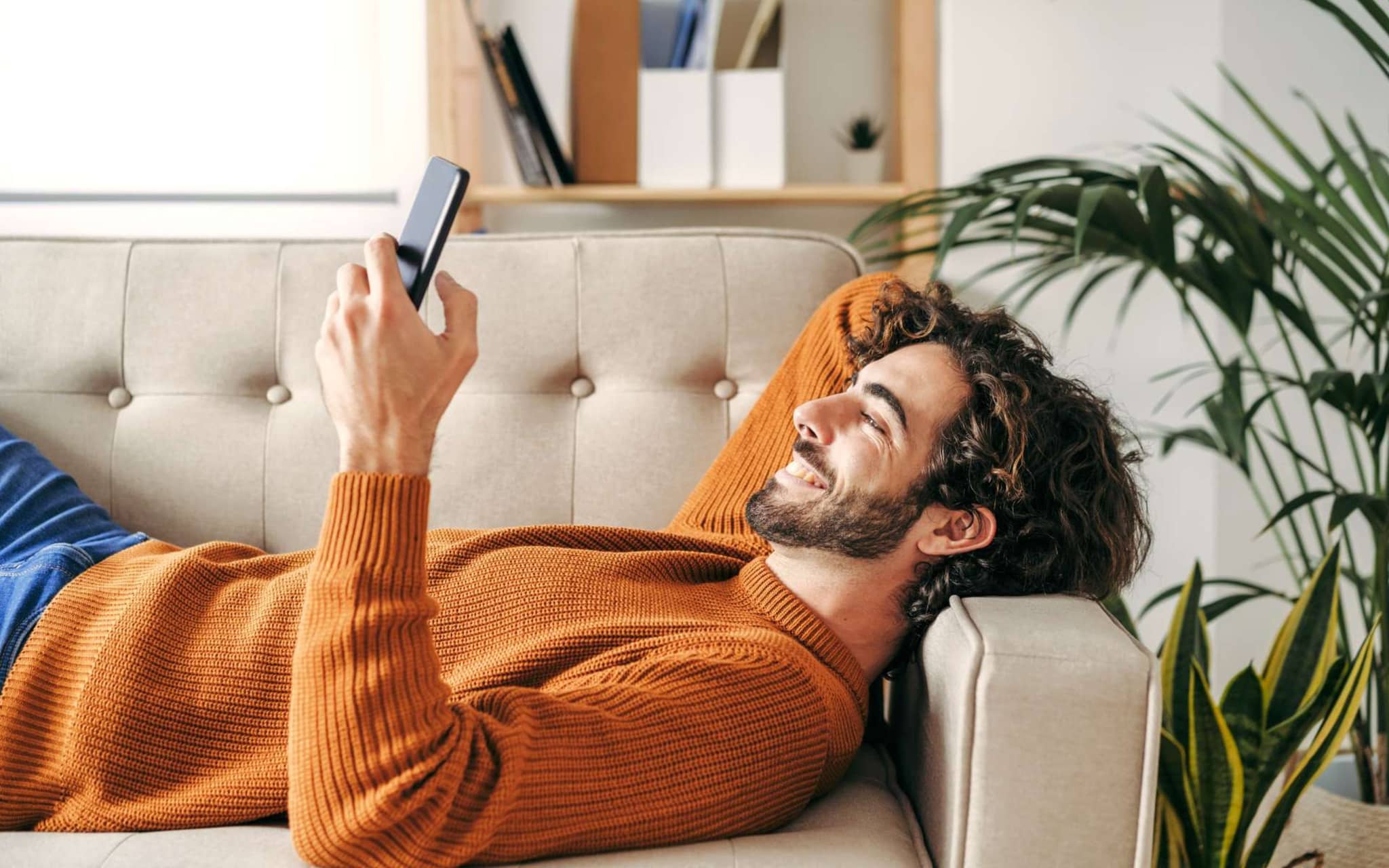 Digitale Angebote: Junger Mann liegt auf dem Sofa und schaut auf sein Handy.