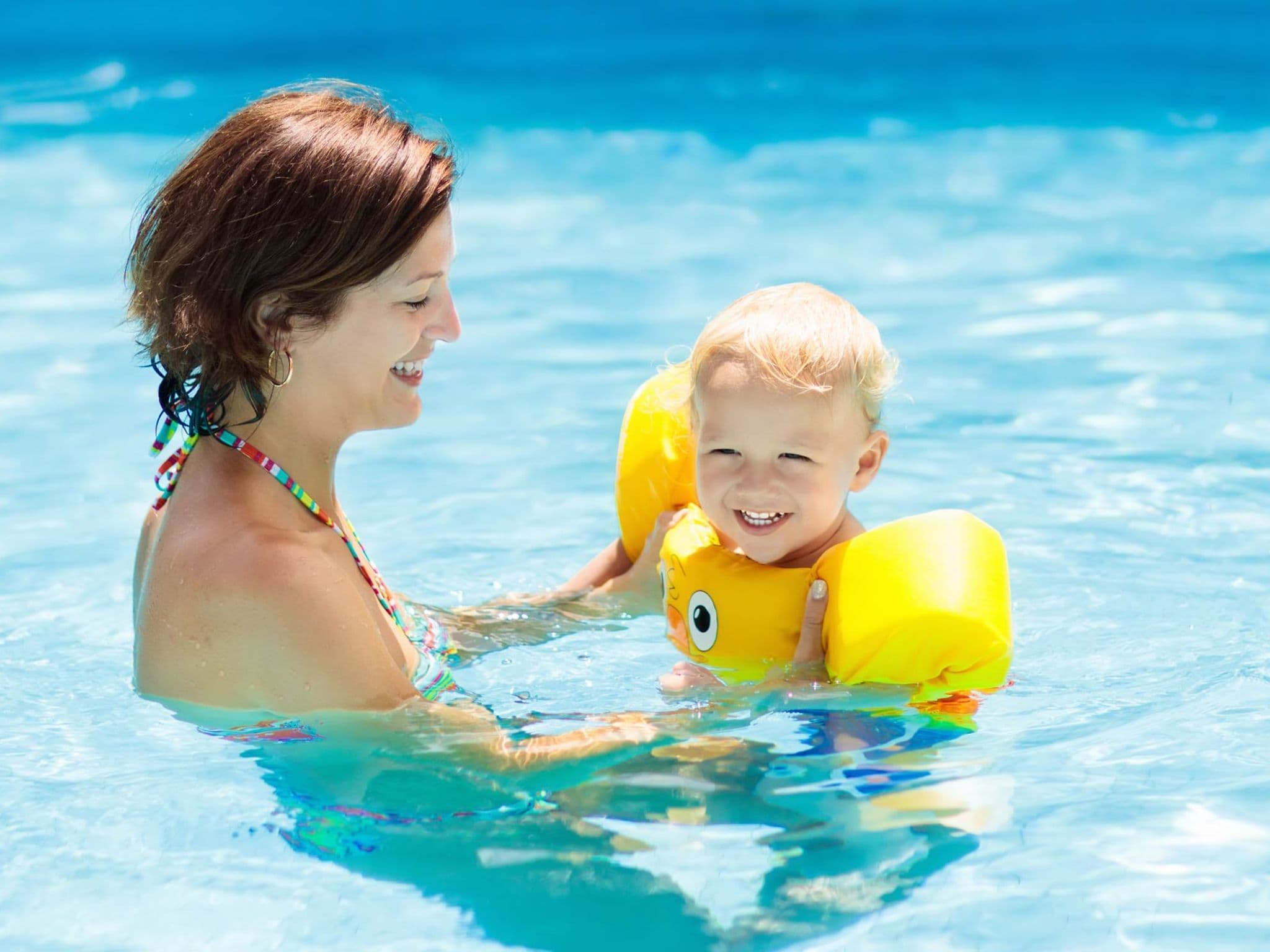 Schwimmen mit Kleinkind: Eine Mutter übt mit ihrem kleinen Kind in einem Freibad schwimmen.