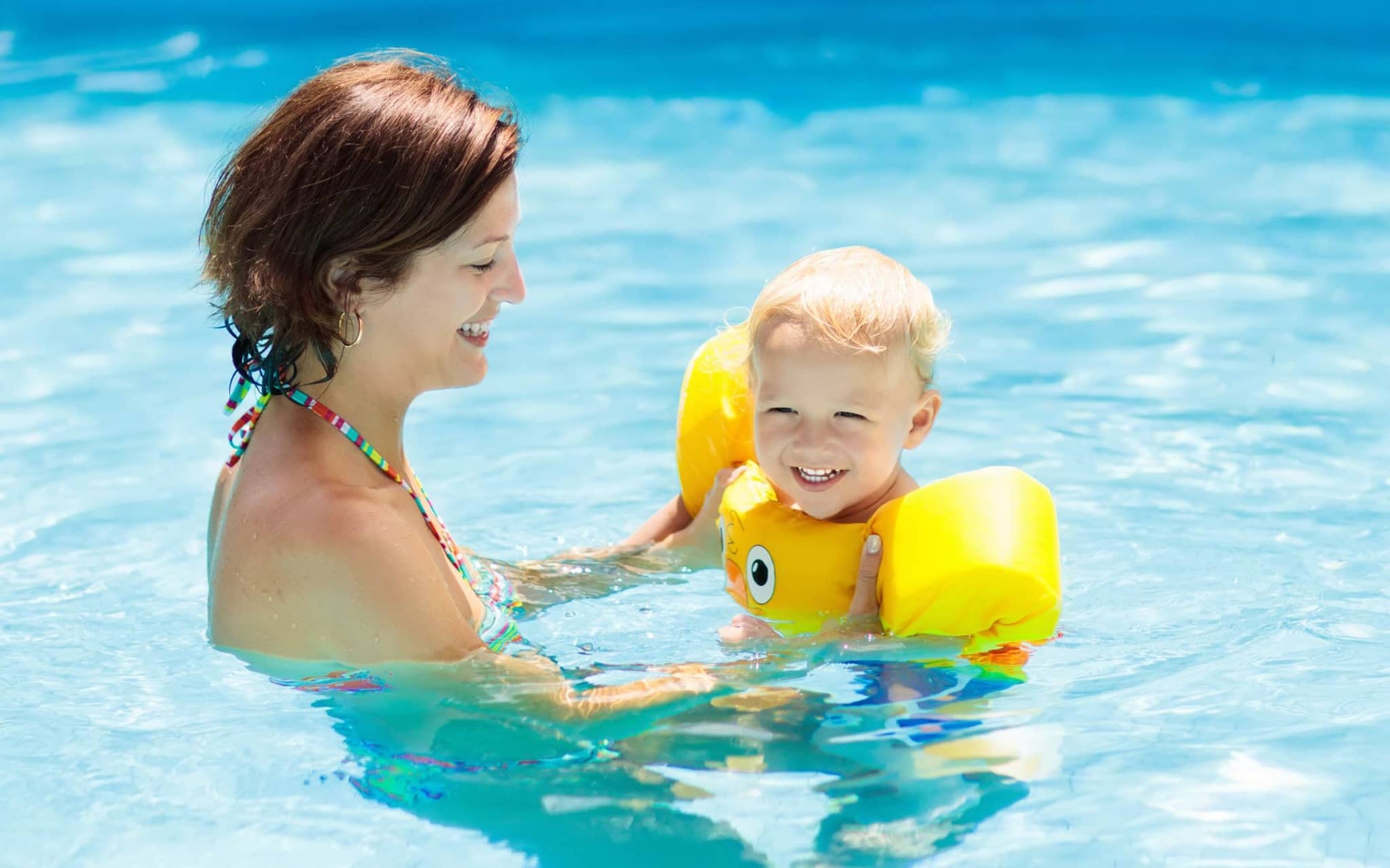 Schwimmen mit Kleinkind: Eine Mutter übt mit ihrem kleinen Kind in einem Freibad schwimmen.