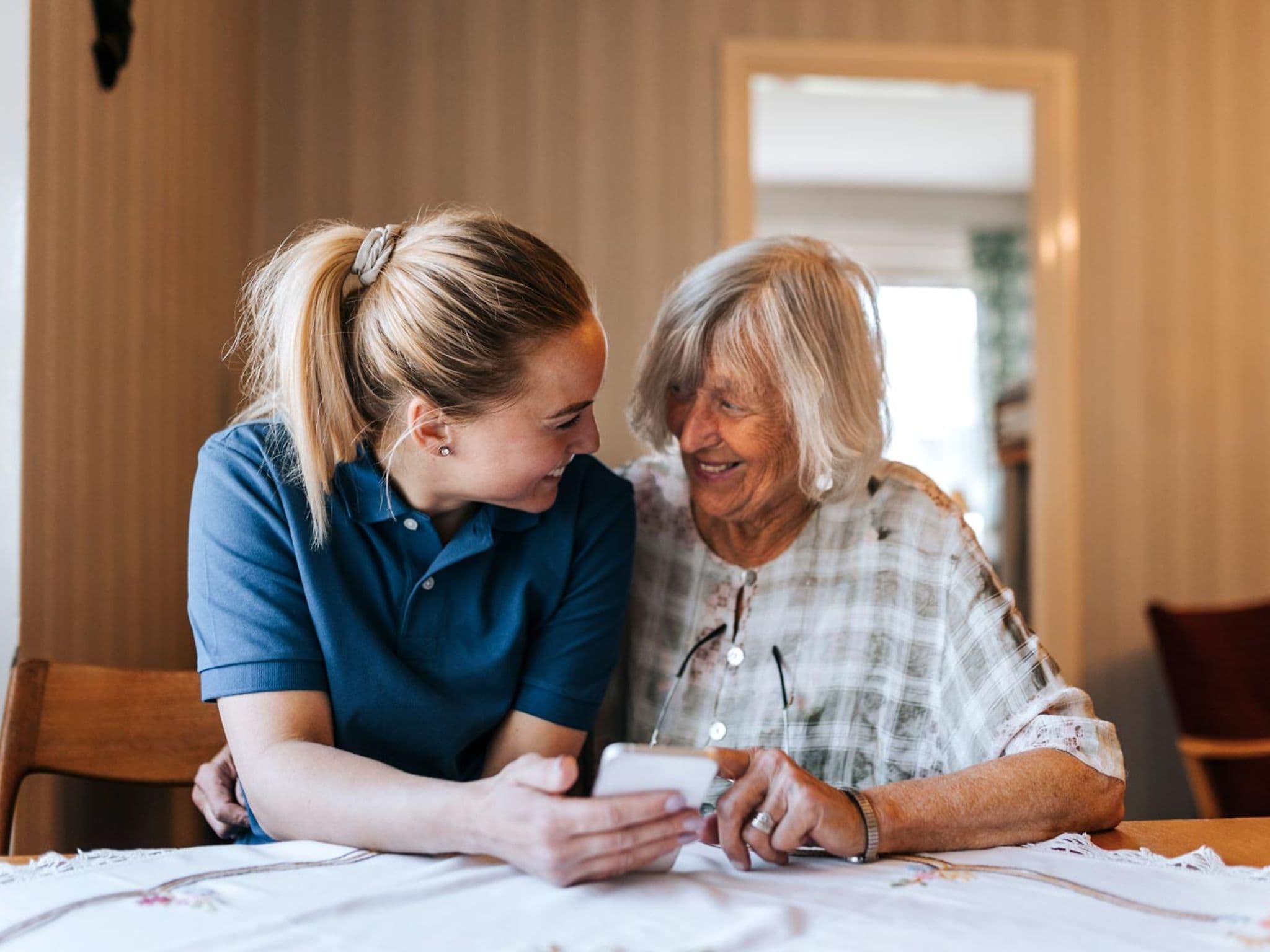 Pflegeleistungen: Pflegerin hilft einer Seniorin bei der Bedienung eines Smartphones.
