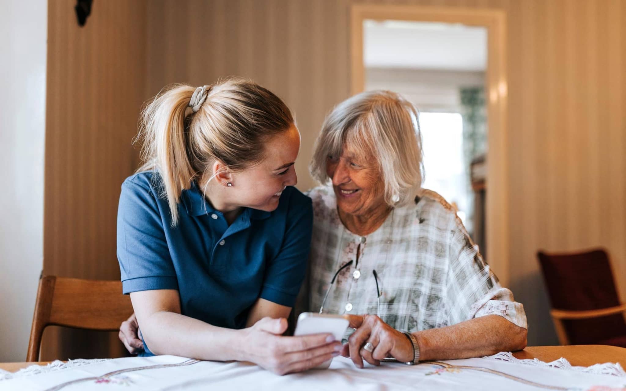 Pflegeleistungen: Pflegerin hilft einer Seniorin bei der Bedienung eines Smartphones.