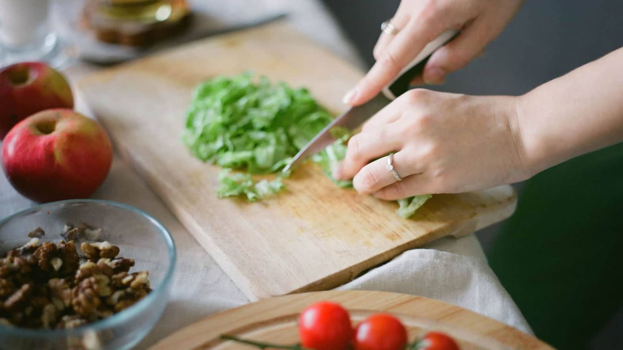 Abnehmkurse: Hände zerkleinern mit Messer Salat, Tomaten liegen daneben.