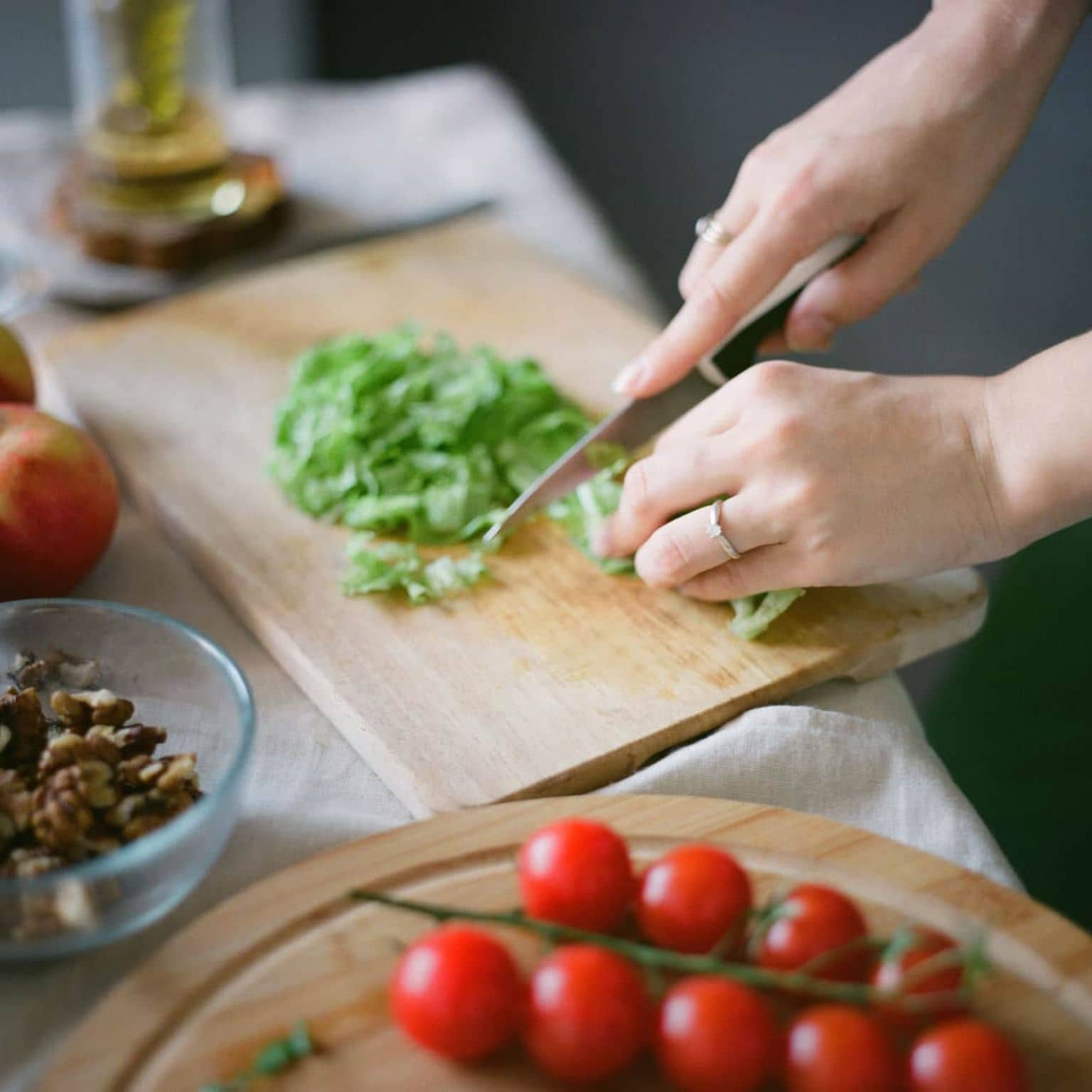 Abnehmkurse: Hände zerkleinern mit Messer Salat, Tomaten liegen daneben.
