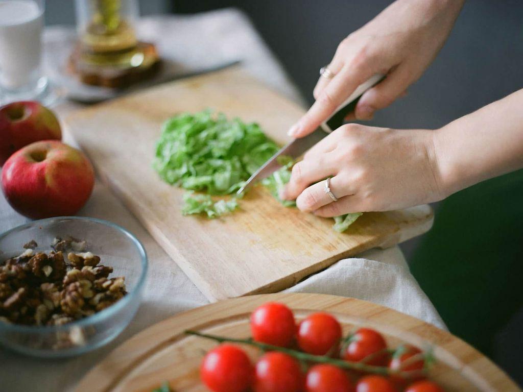 Abnehmkurse: Hände zerkleinern mit Messer Salat, Tomaten liegen daneben.