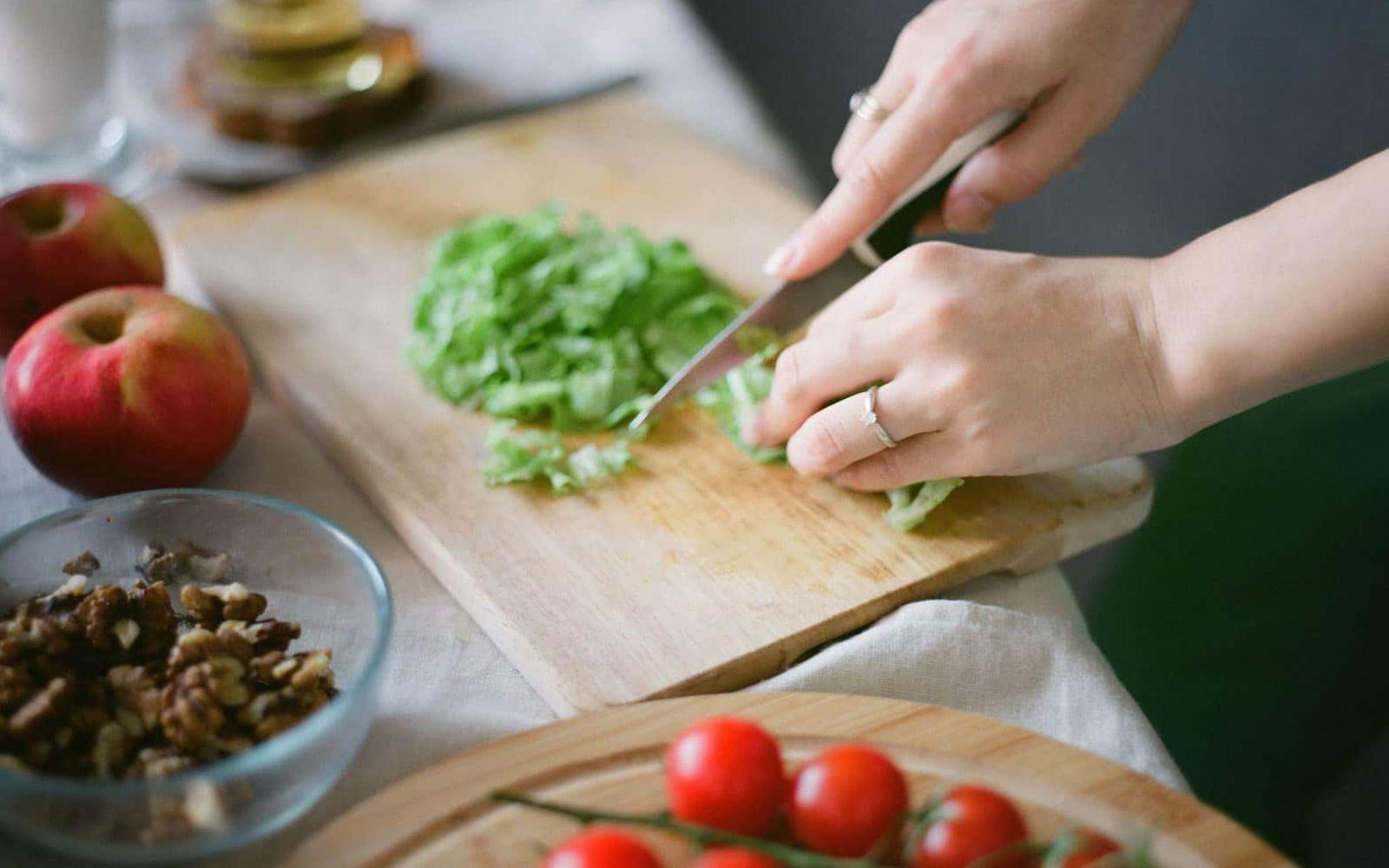 Abnehmkurse: Hände zerkleinern mit Messer Salat, Tomaten liegen daneben.