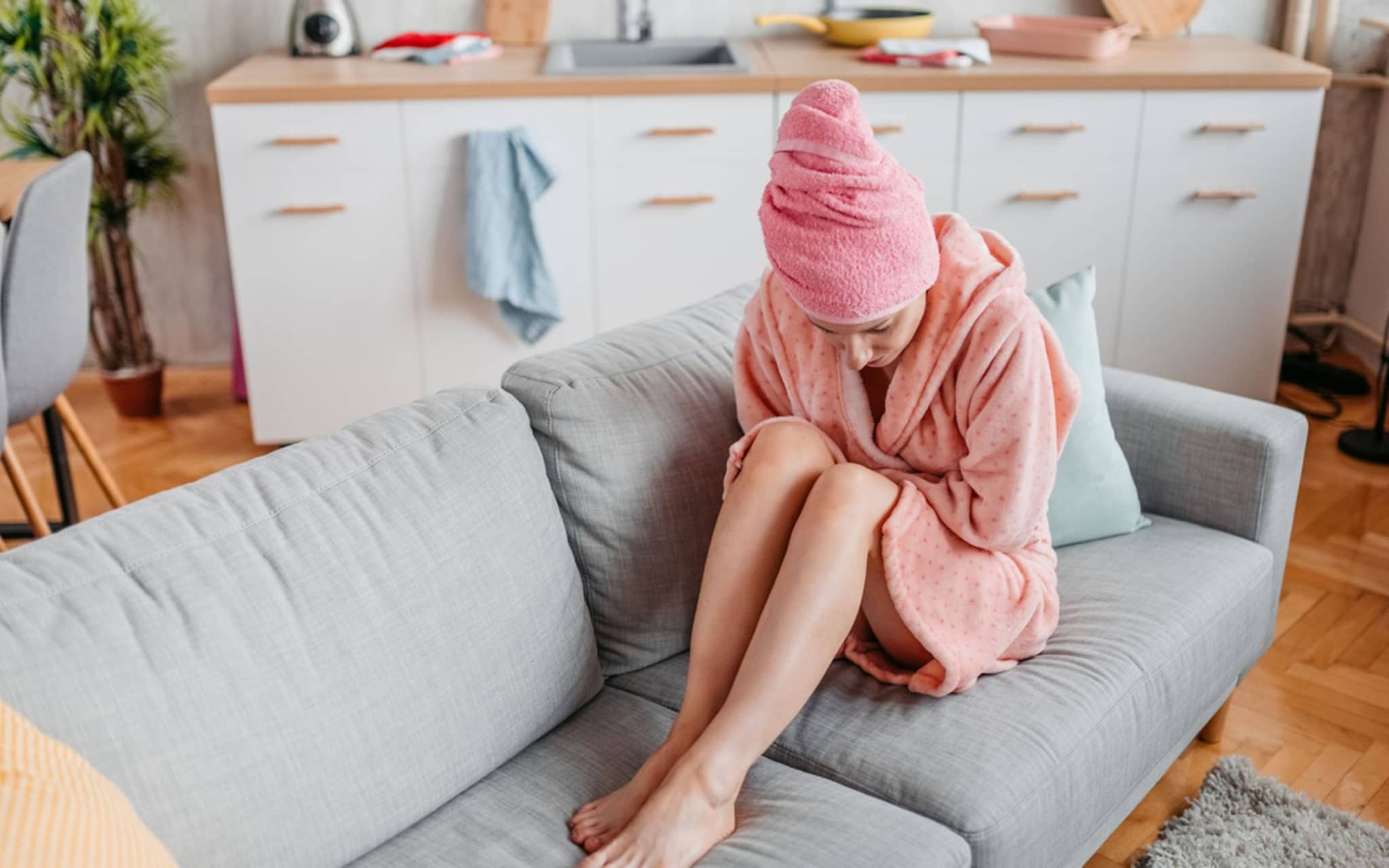 Darmgesundheit: Eine junge Frau sitzt im Bademantel auf dem Sofa und krümmt sich vor Bauchschmerzen.