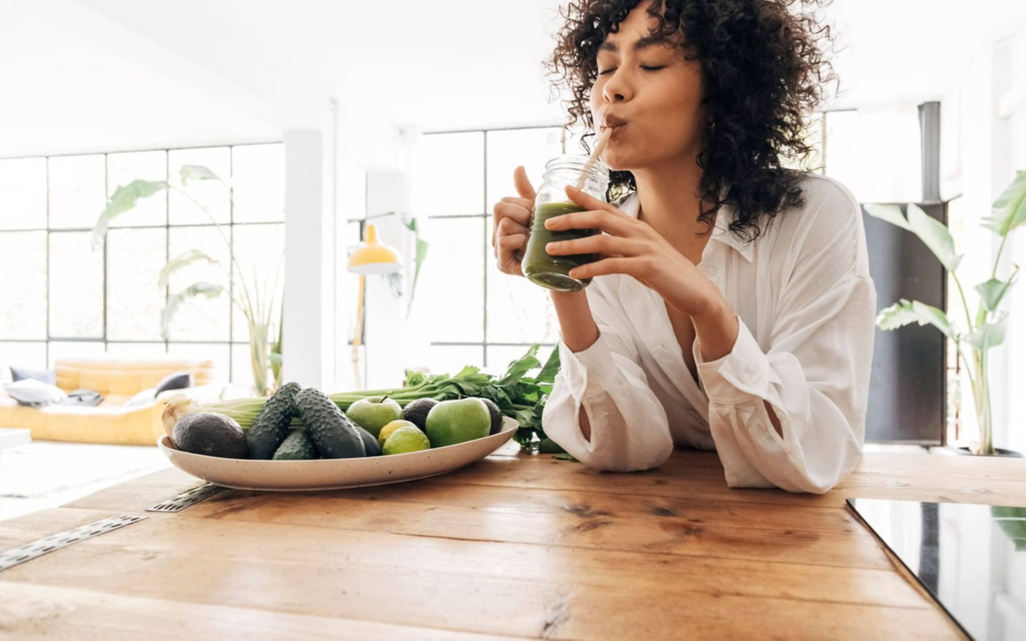 Darmgesundheit: Junge Frau sitzt am Esstisch und trinkt einen Smoothie.