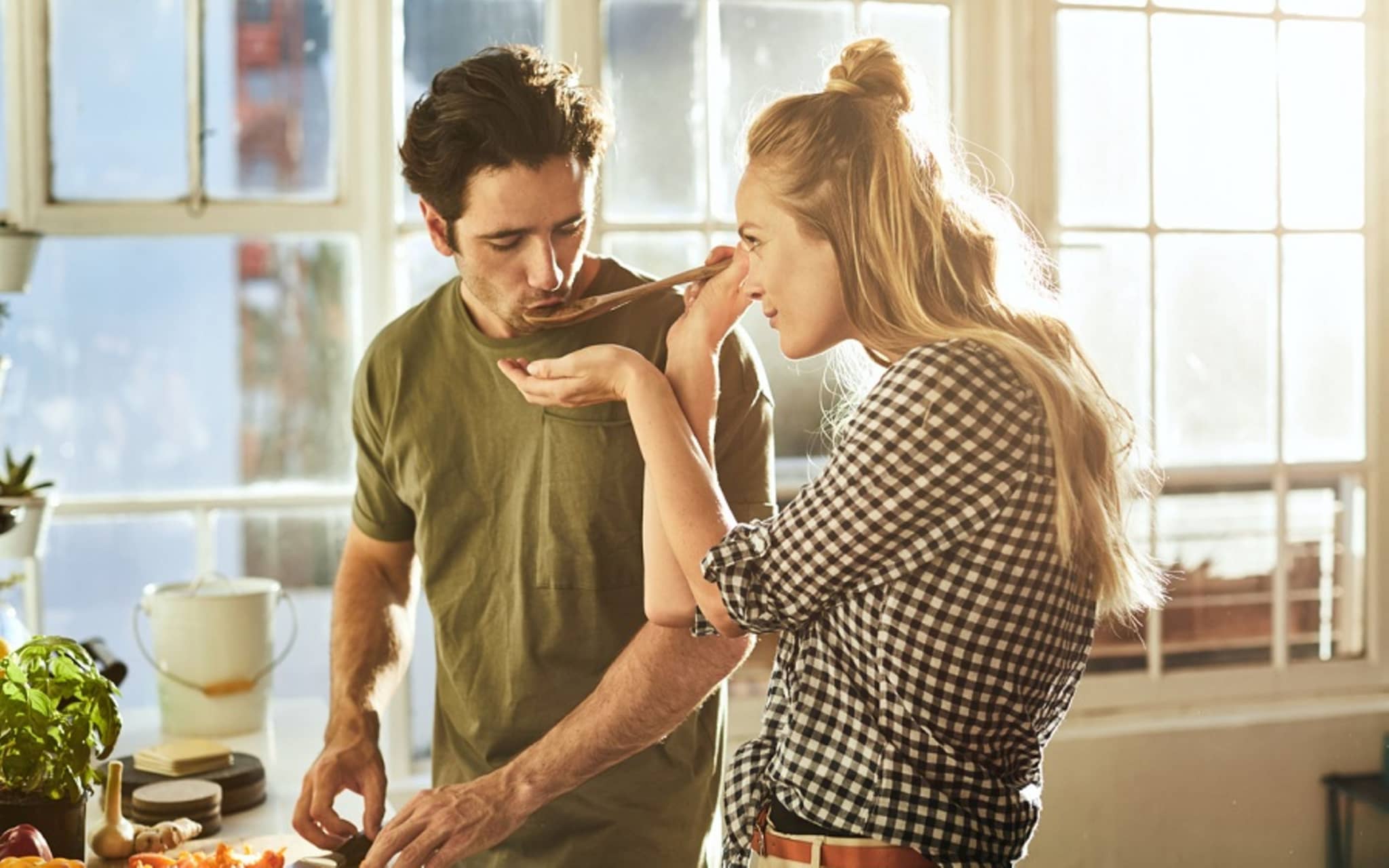 Ernährungskurse: Frau hält Mann Kochlöffel vor den Mund, damit er das Essen probiert.