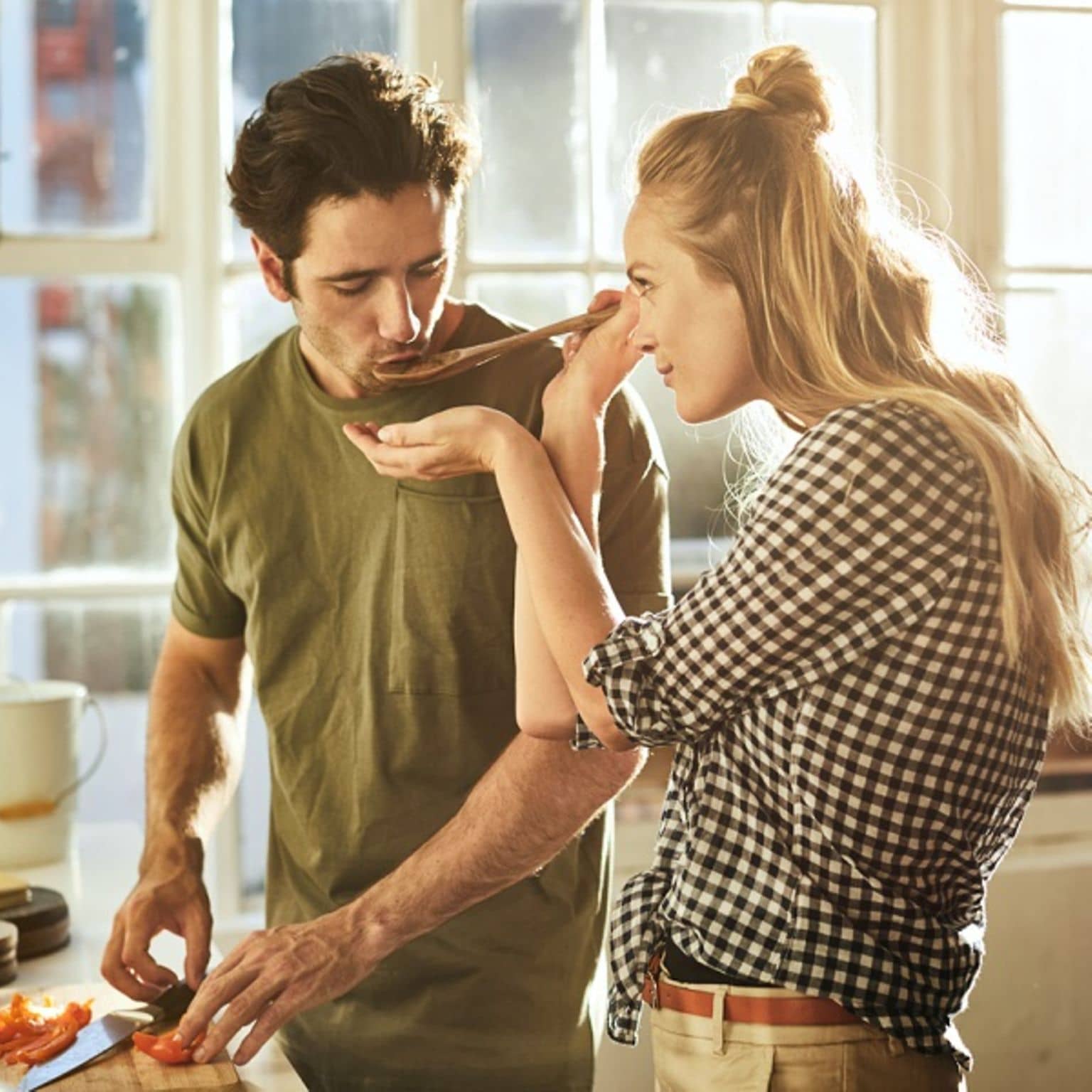 Ernährungskurse: Frau hält Mann Kochlöffel vor den Mund, damit er das Essen probiert.