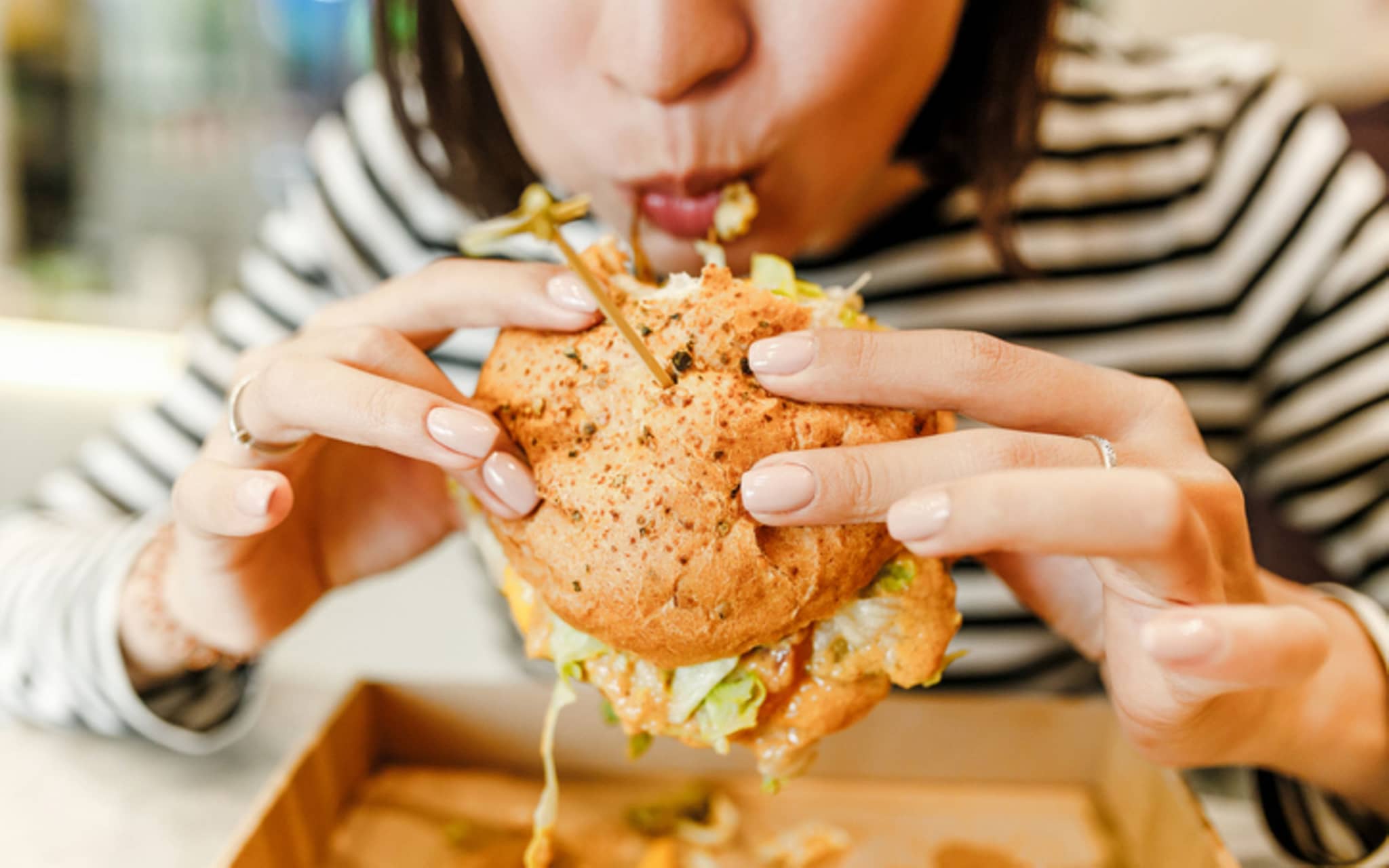 Ungesund für den Darm: Frau beißt in einen üppig belegten Hamburger.