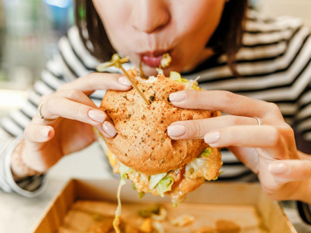Ungesund für den Darm: Frau beißt in einen üppig belegten Hamburger.
