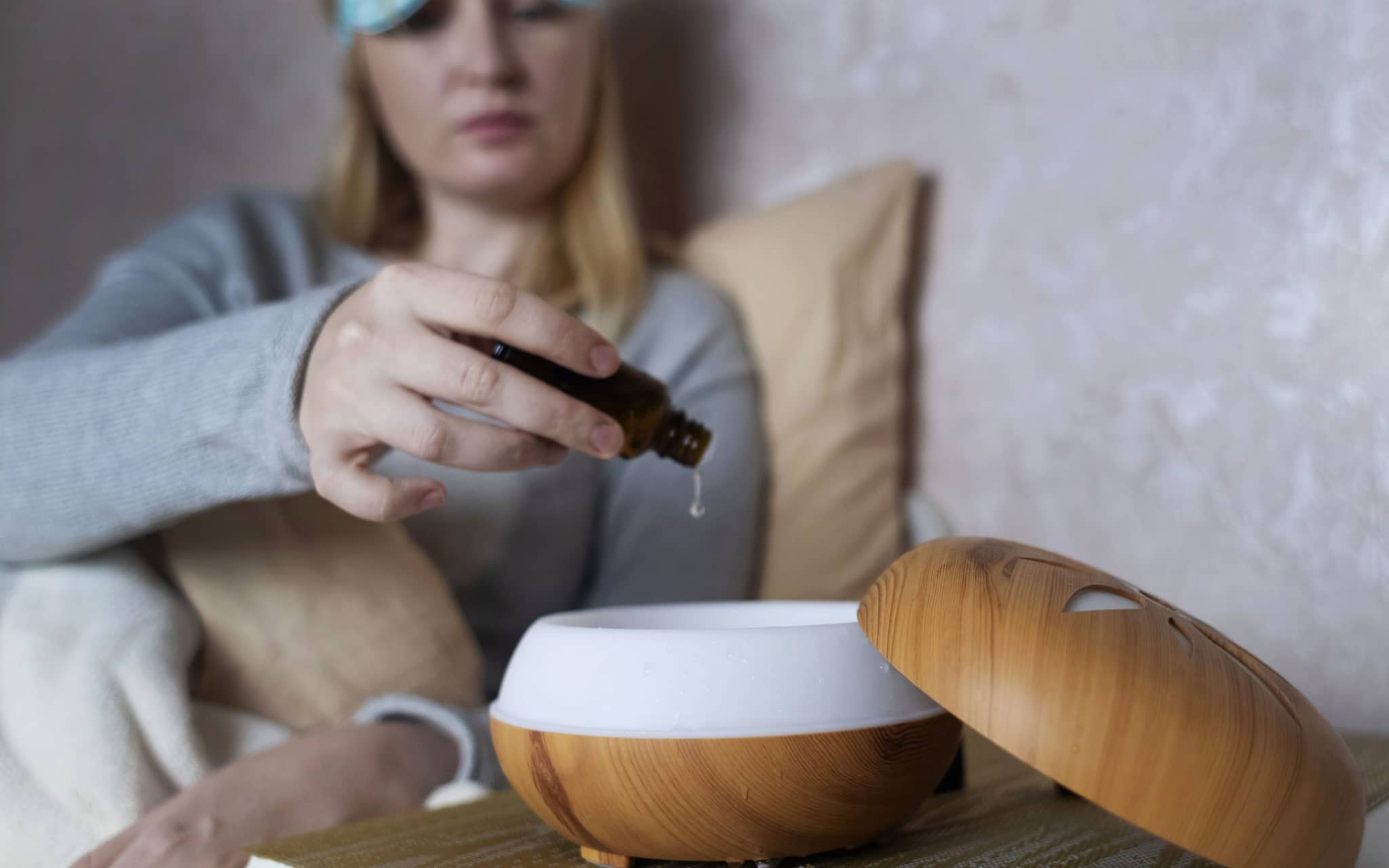 Raumduft Schlafzimmer: Eine Frau sitzt auf einem Bett und gibt Öl in einen Defuser