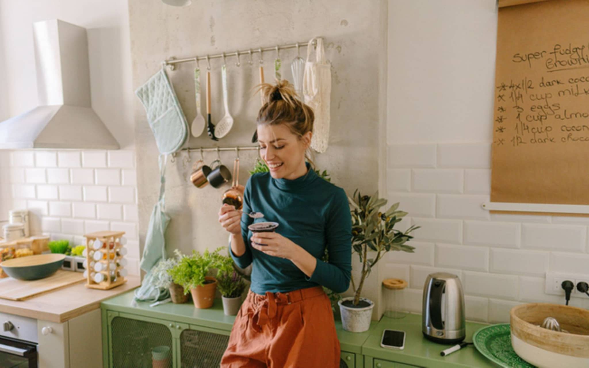 Darm und Psyche: Junge Frau steht in der Küche uns isst einen Joghurt.