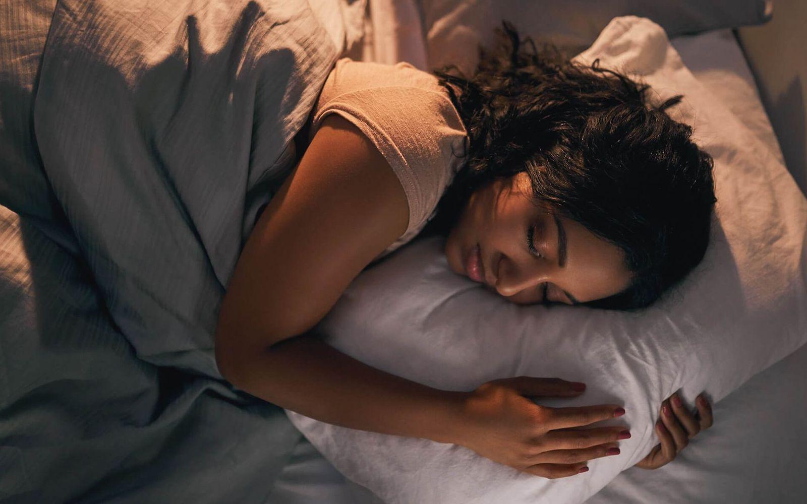 Schlafphasen: Junge Frau, die im Bett schläft und ihr Kissen umarmt