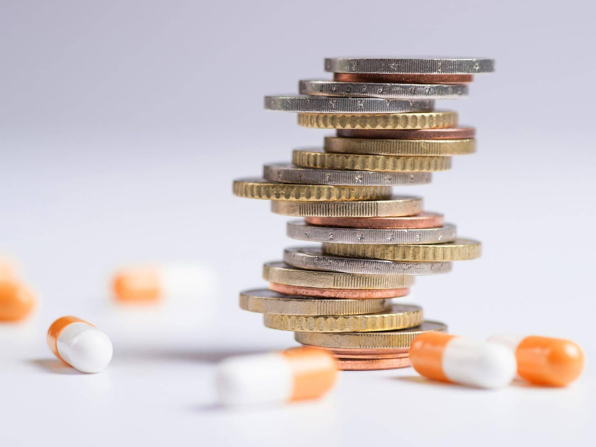 AMNOG-Report 2025: Mehrere Tabletten liegen verstreut um einen Stapel Münzen herum.