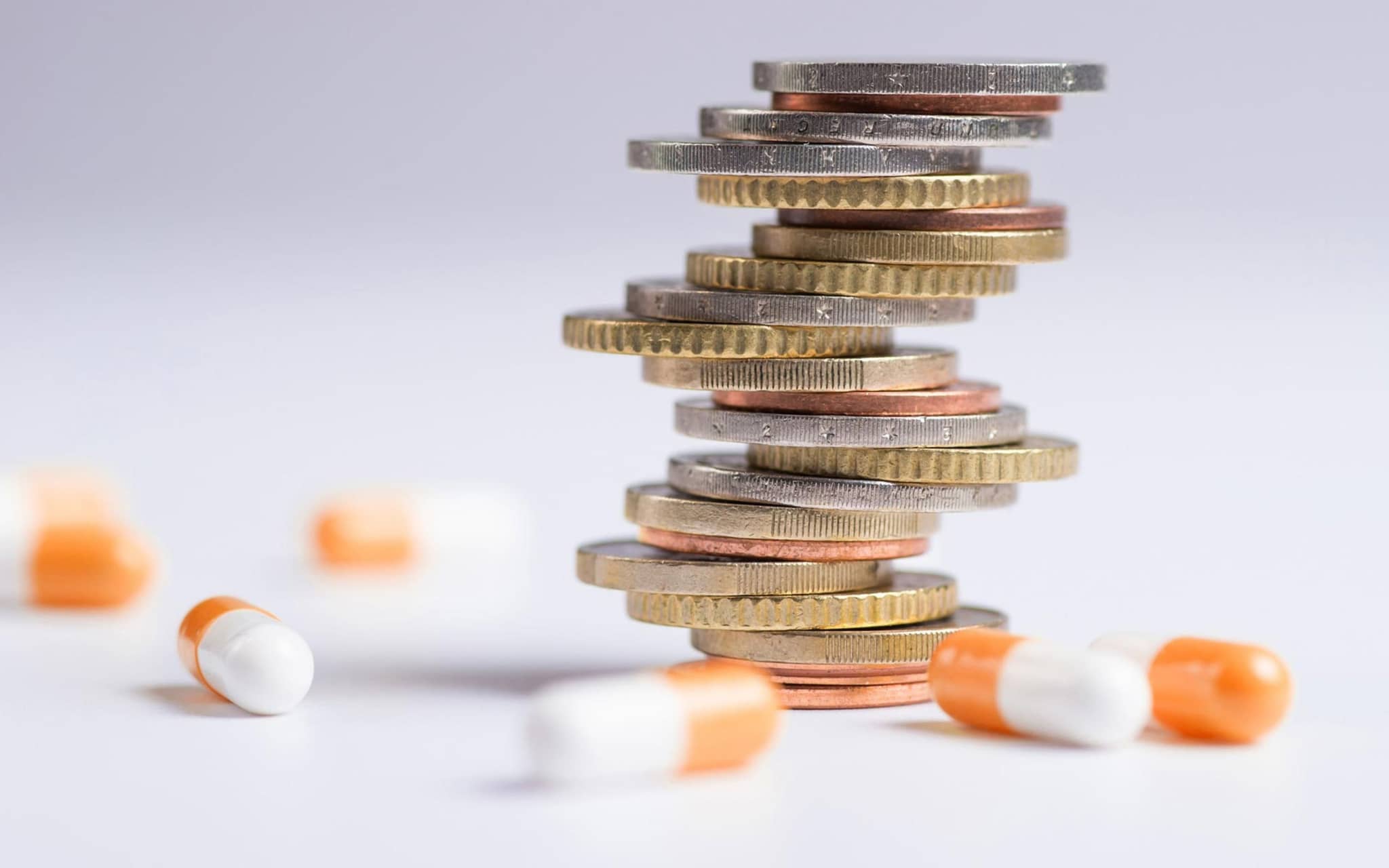 AMNOG-Report 2025: Mehrere Tabletten liegen verstreut um einen Stapel Münzen herum.