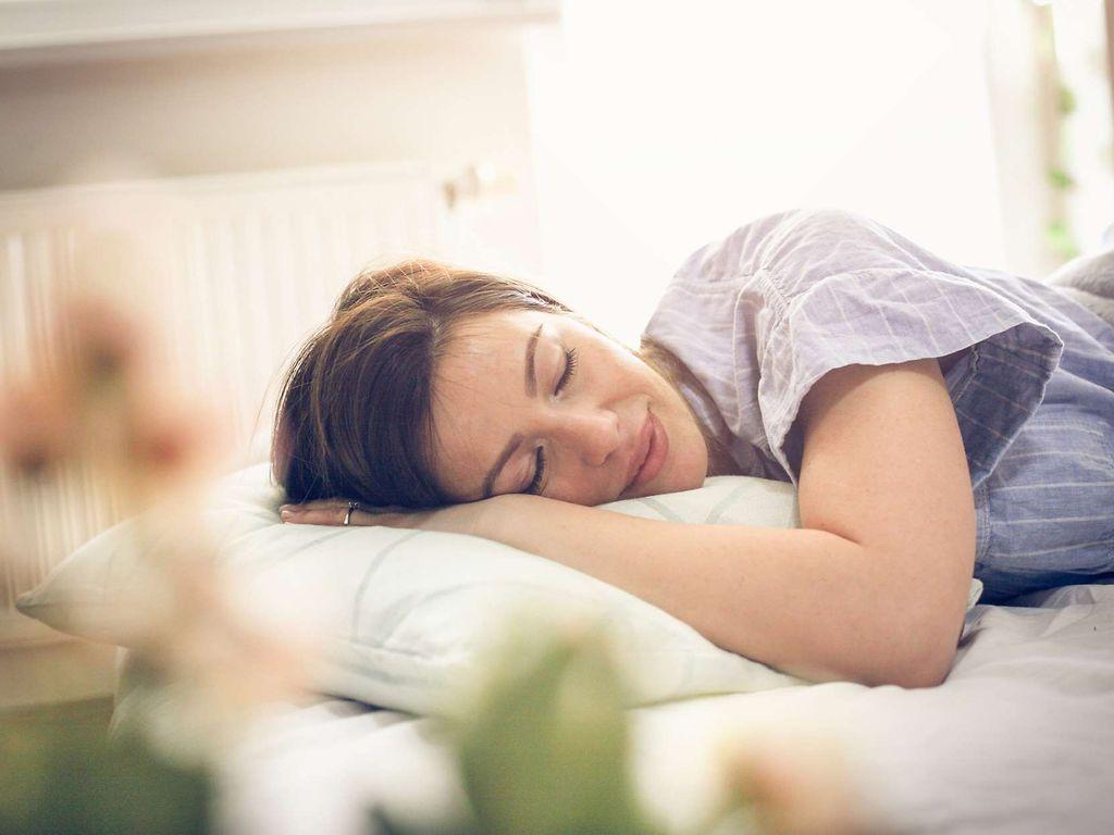 Meditation gegen Schlafstörungen: Frau schläft entspannt in ihrem Bett.