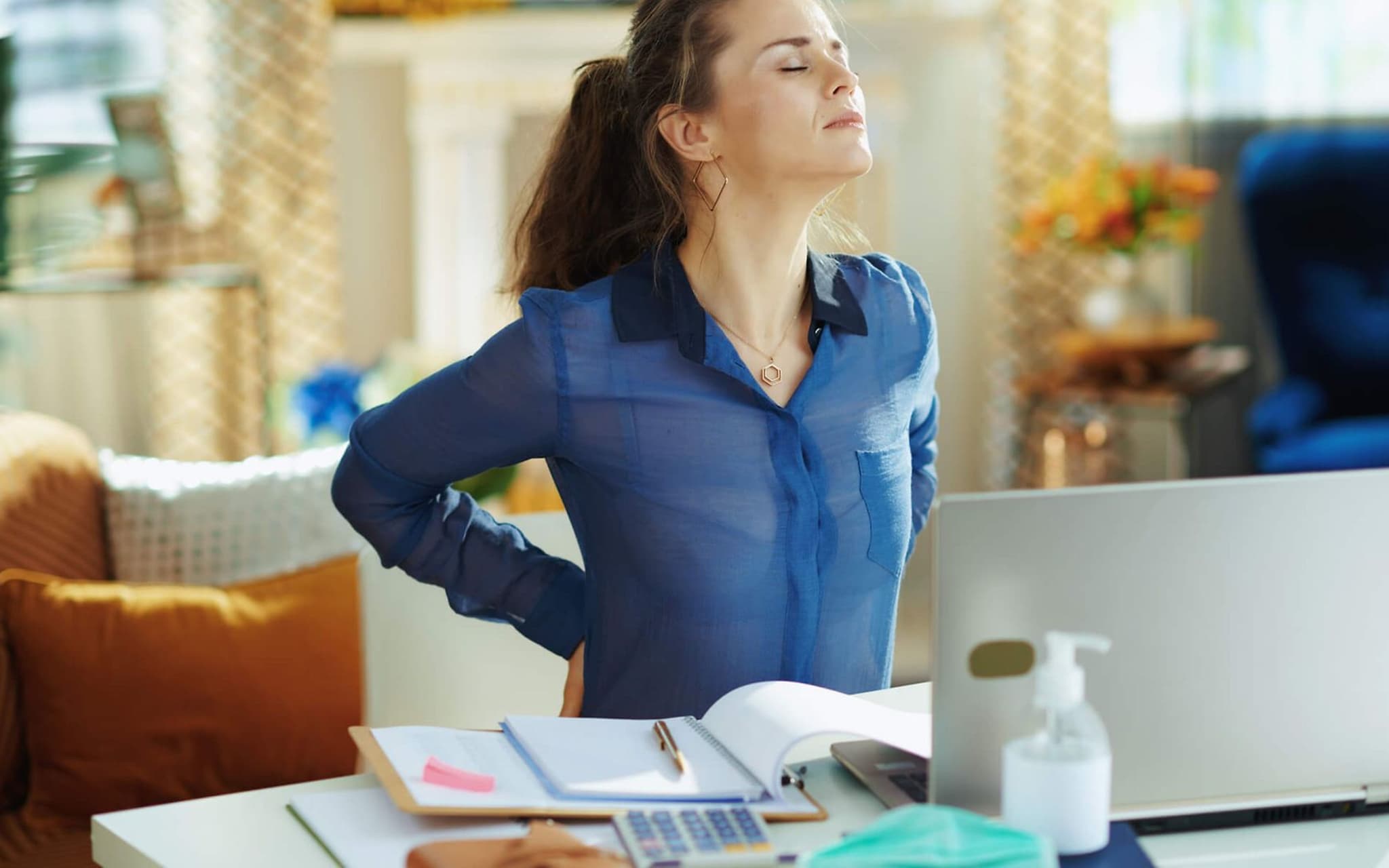 Junge Frau mit Rückenschmerzen am Schreibtisch
