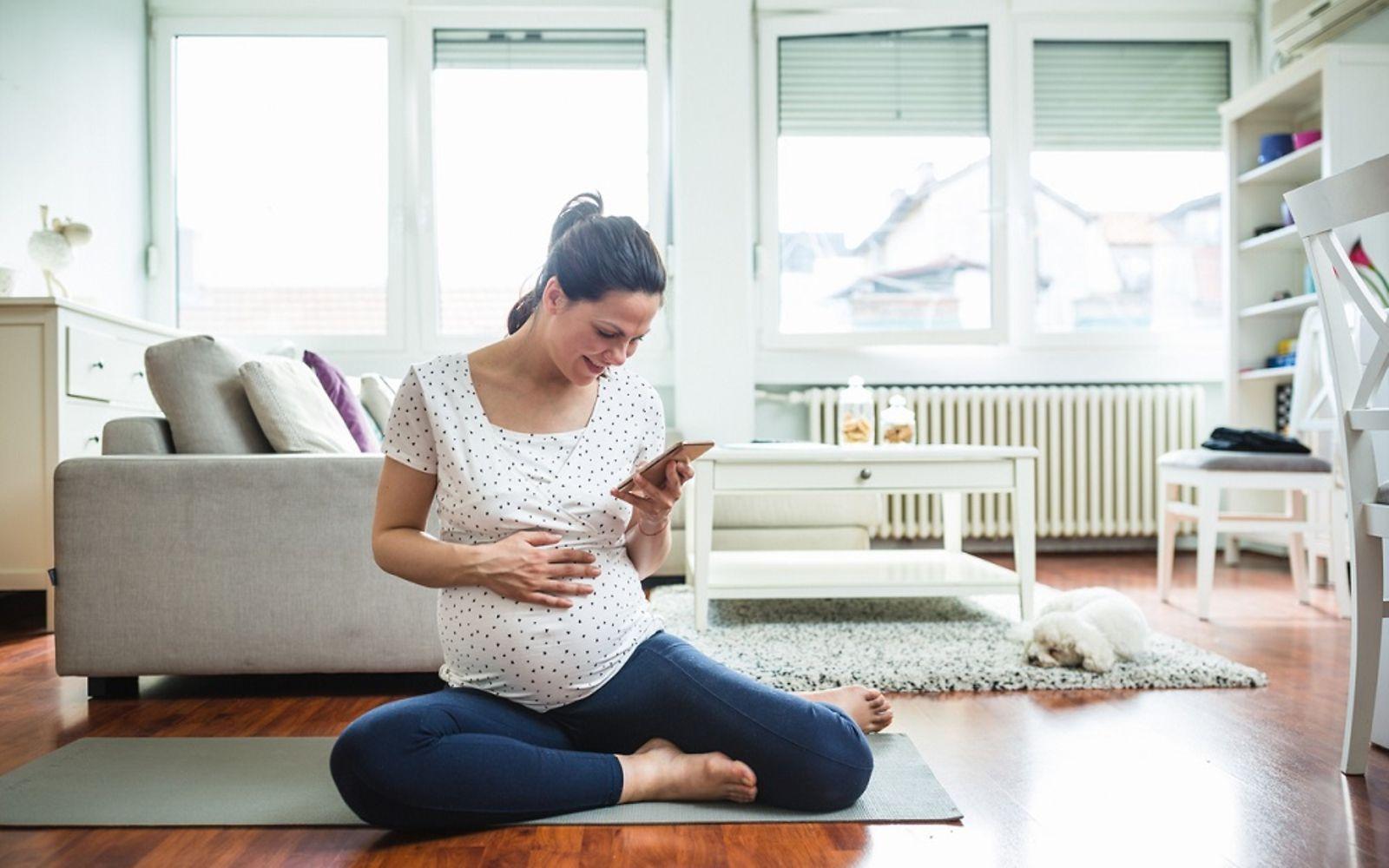 DAK Schwangerschaftscoaching: Schwangere sitzt auf dem Boden mit Handy in der Hand.