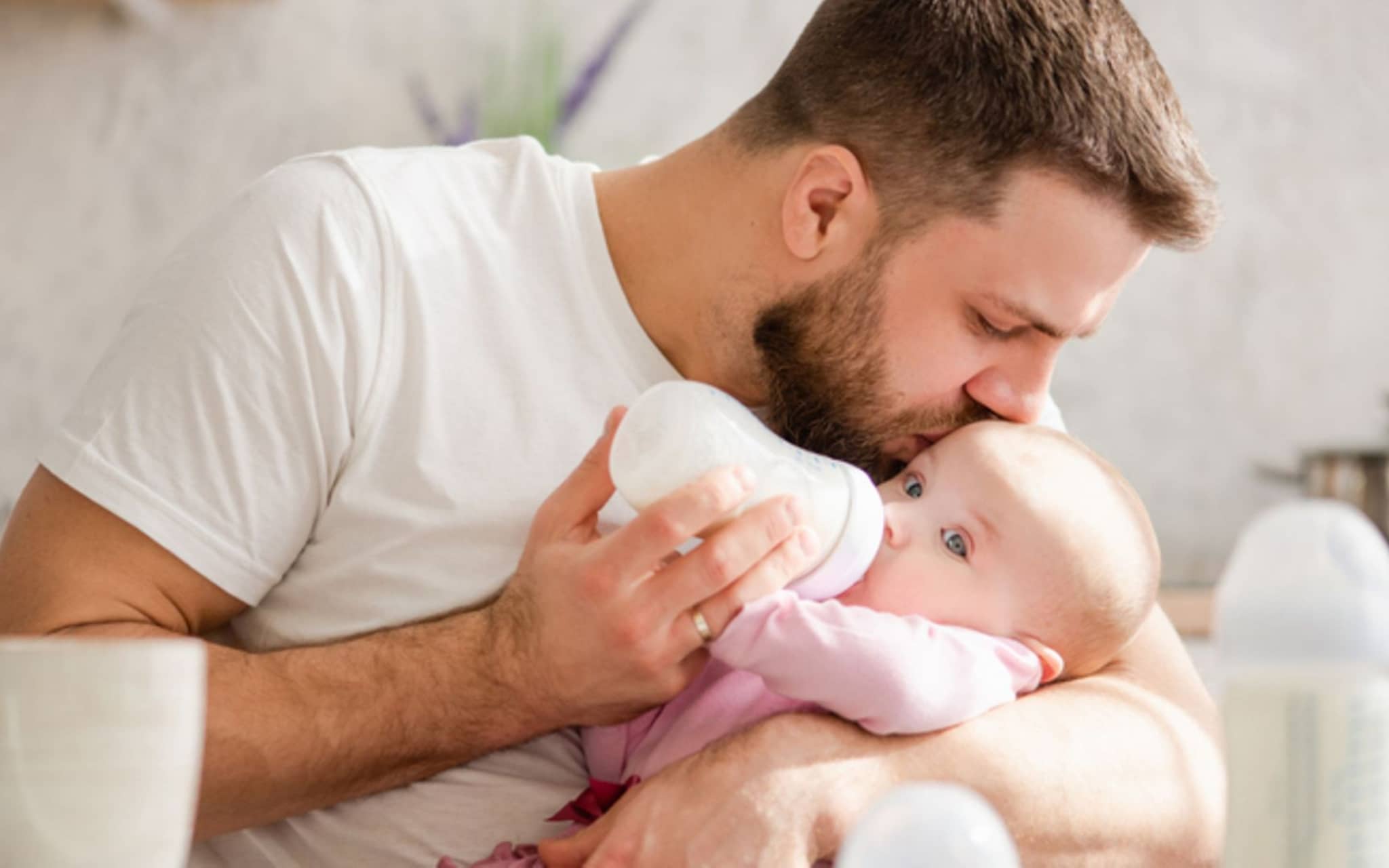 Säuglingsmilchnahrung: Vater küsst Baby beim Füttern mit der Flasche auf die Stirn