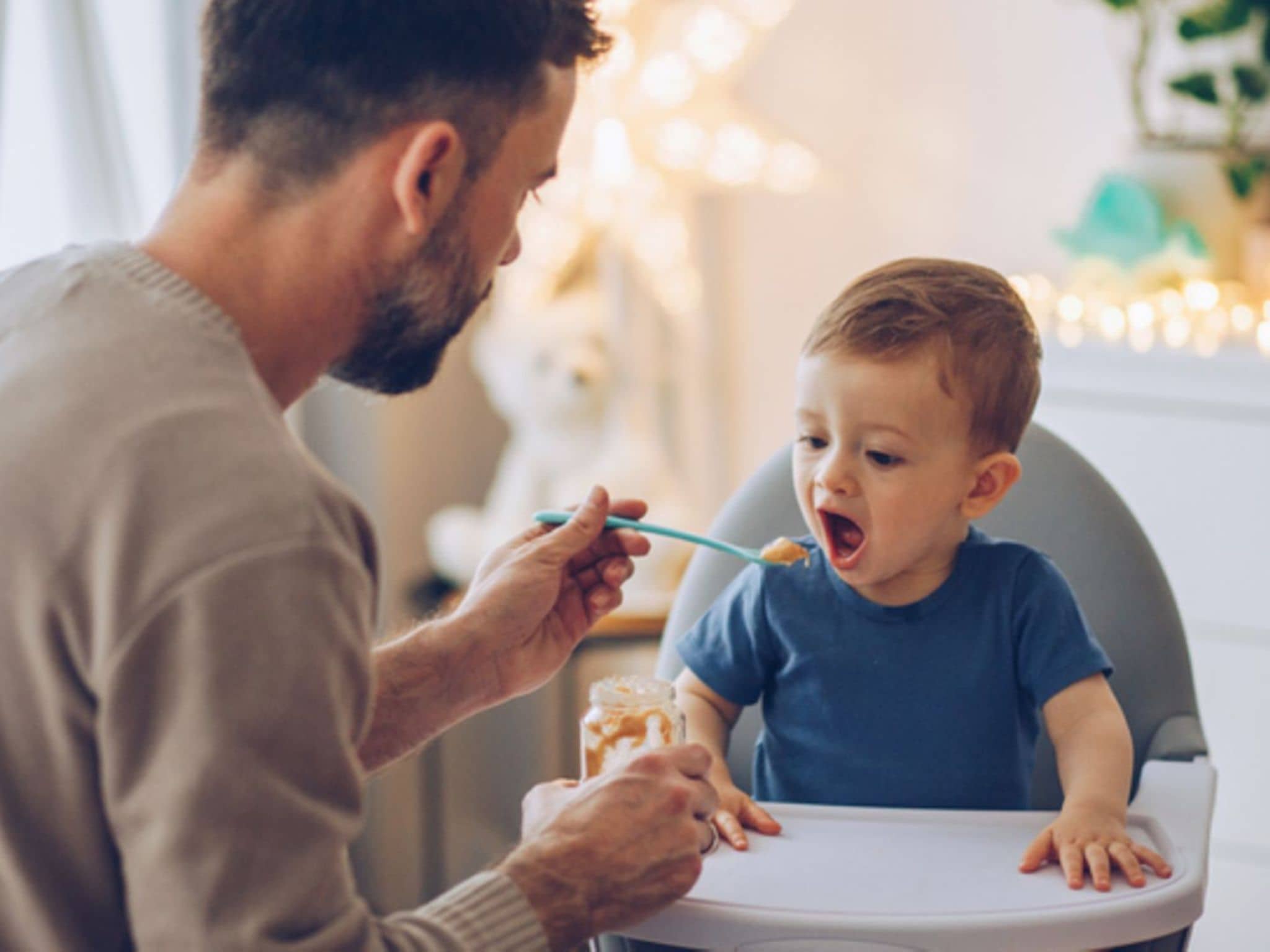 Beikosteinführung: Ein kleiner Junge wird von seinem Vater im Hochstuhl mit Brei gefüttert