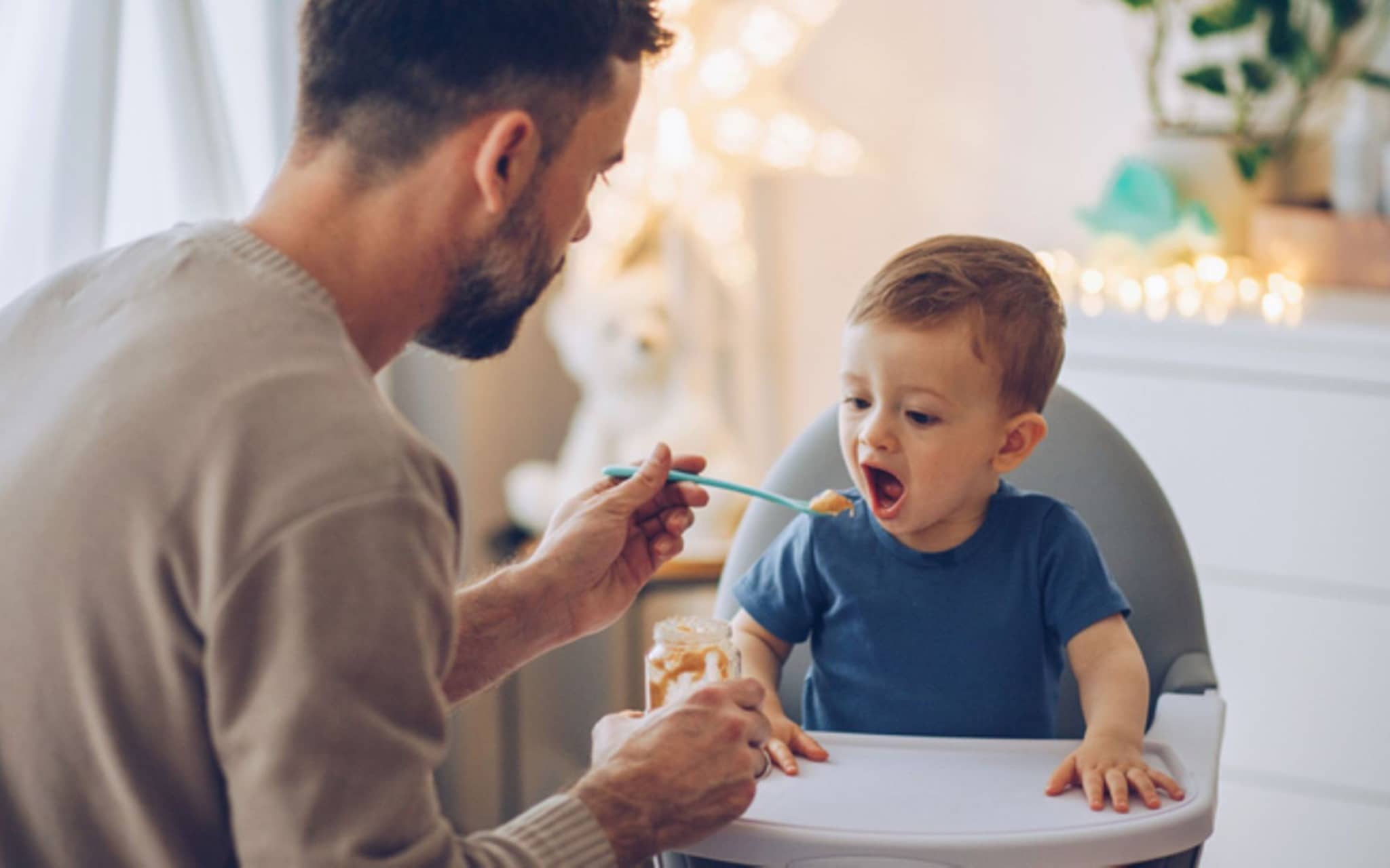 Beikosteinführung: Ein kleiner Junge wird von seinem Vater im Hochstuhl mit Brei gefüttert