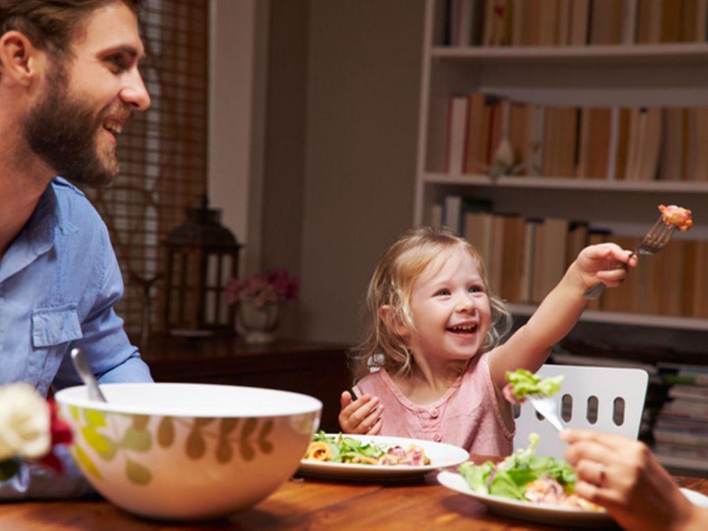Ernährung für Kleinkinder: Junge Familie sitzt amüsiert am Esstisch und isst Salat