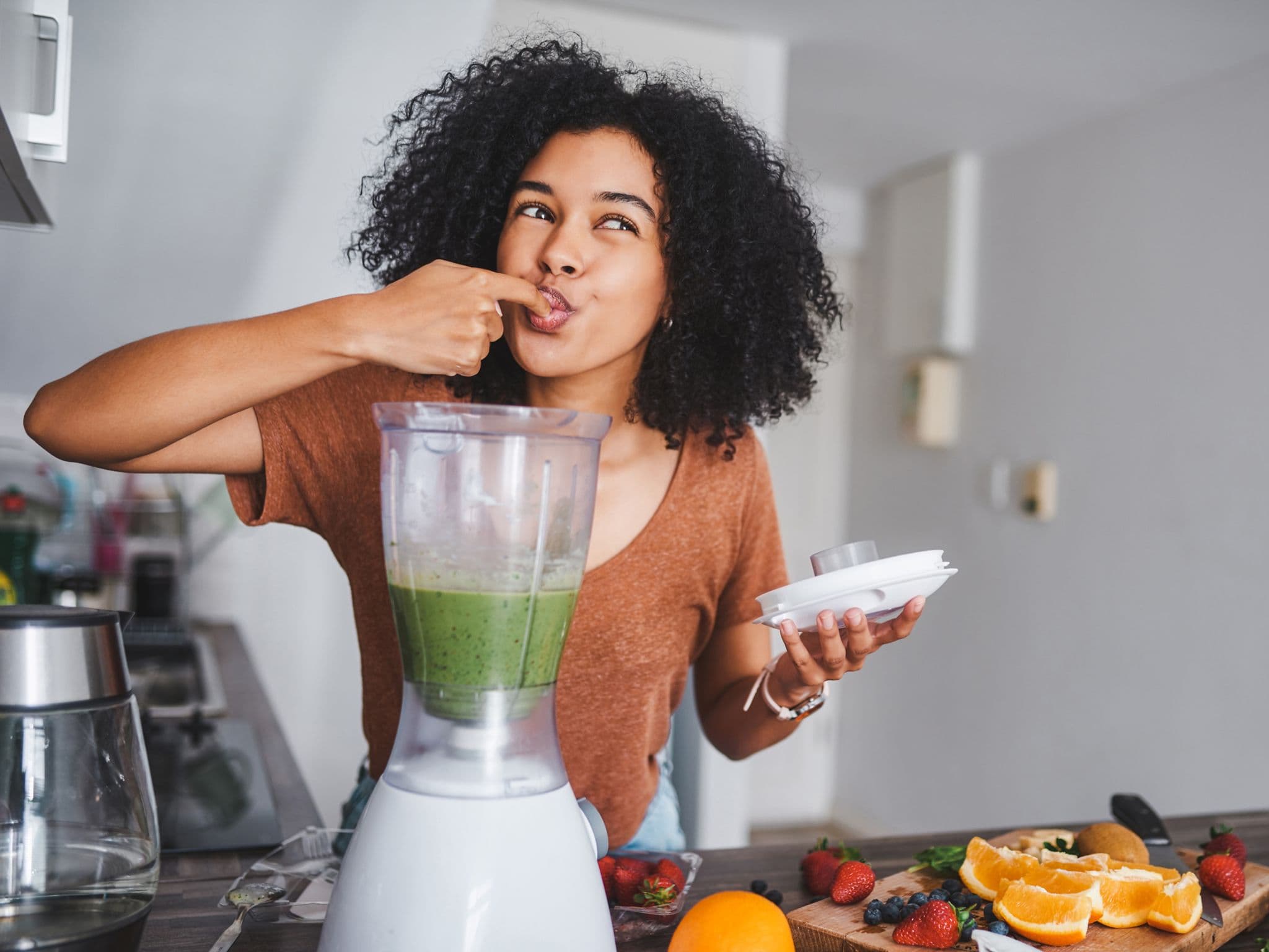 Eine junge Frau leckt den gesunden, frisch zubereiteten Smoothie von ihrem Finger ab.
