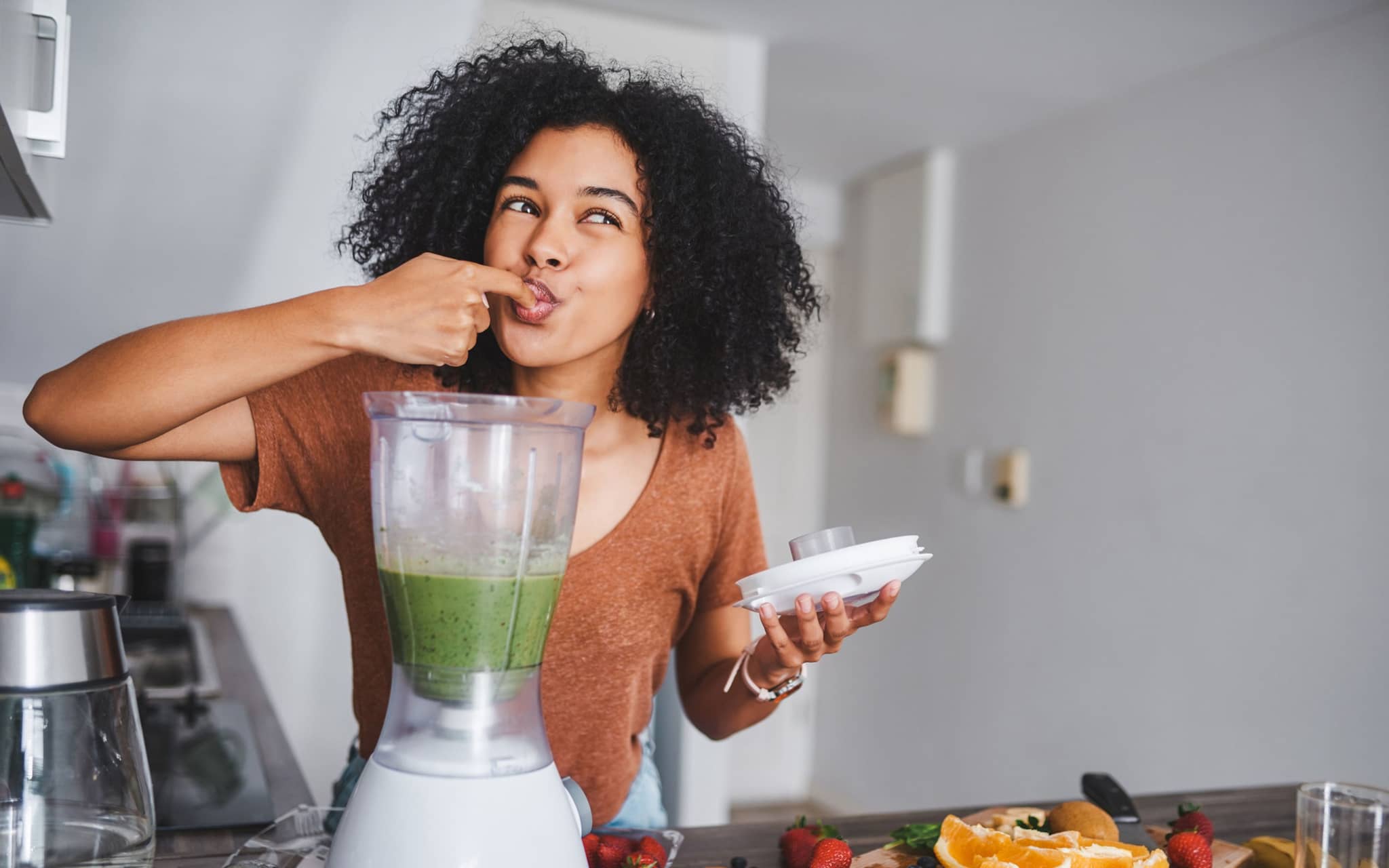 Eine junge Frau leckt den gesunden, frisch zubereiteten Smoothie von ihrem Finger ab.
