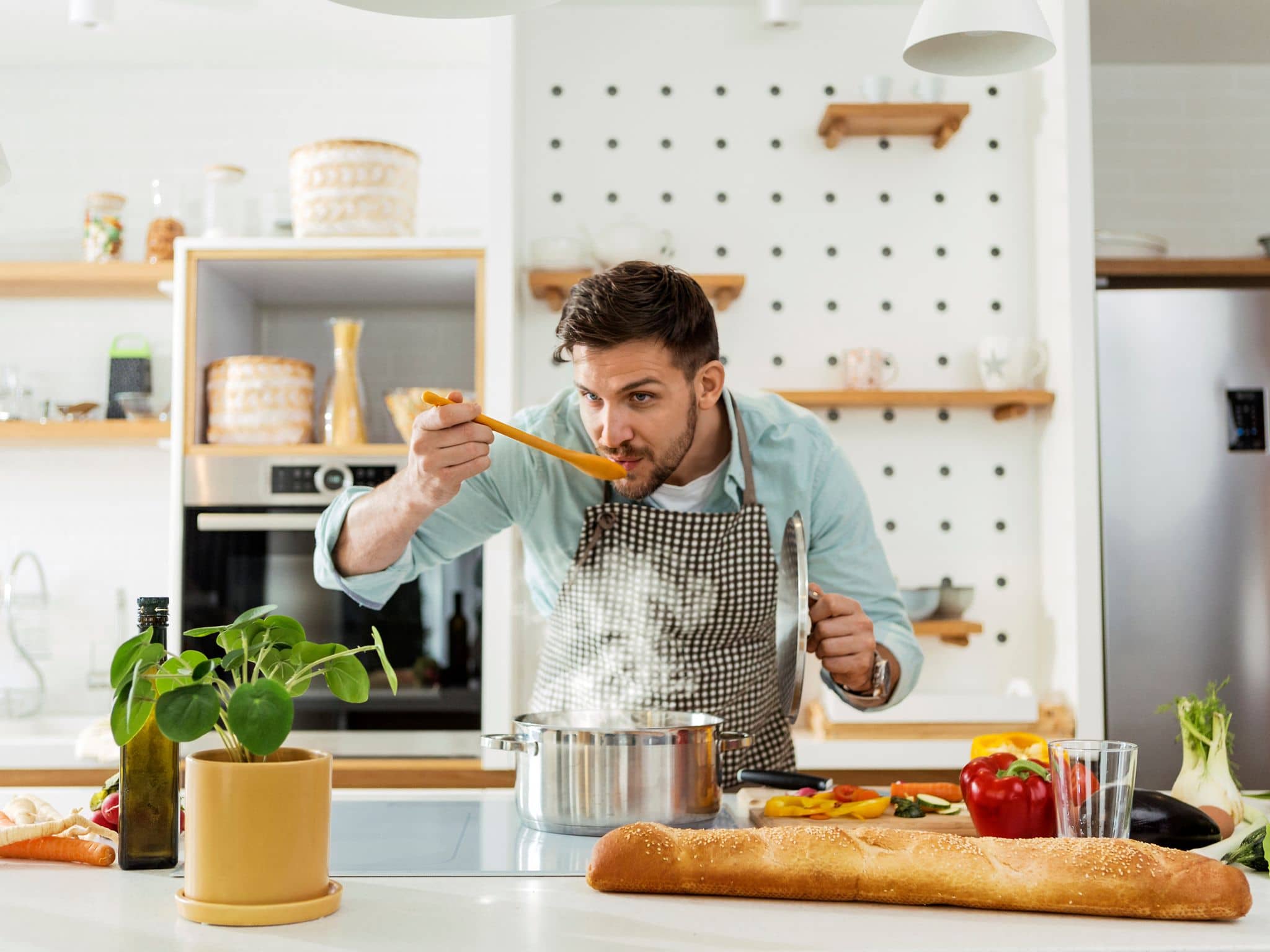 Ein Mann steht in der Küche und probiert sein selbst zubereitetes One-Pot-Gericht mit einem Holzlöffel.