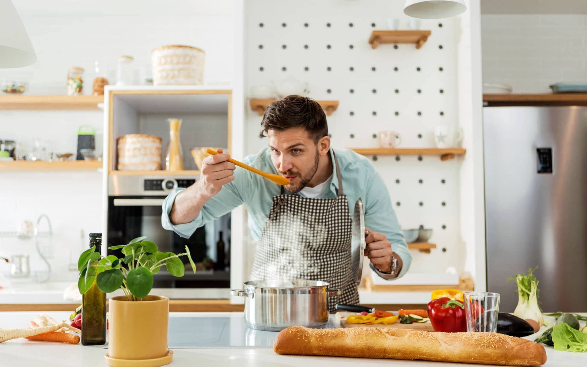 Ein Mann steht in der Küche und probiert sein selbst zubereitetes One-Pot-Gericht mit einem Holzlöffel.