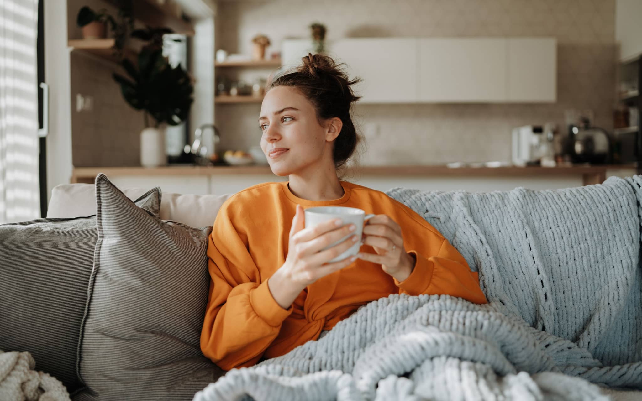 Herzförmige Gebärmutter: Eine junge Frau sitzt gemütlich auf einem Sofa und hält einen Becher in der Hand