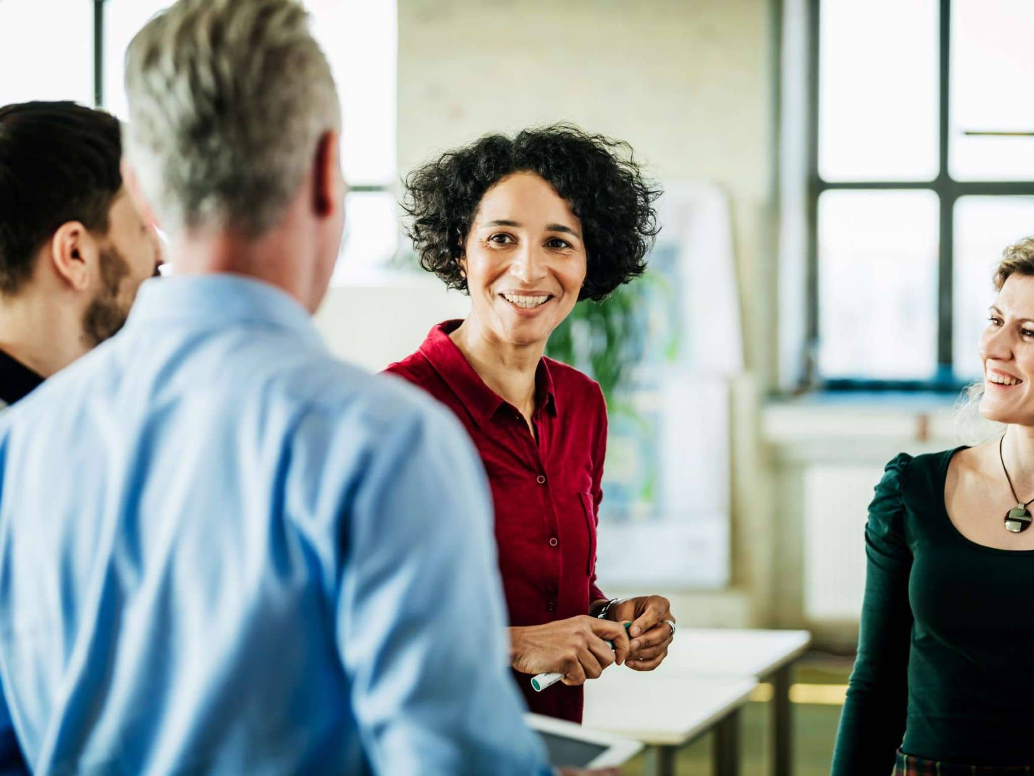 Harmoniebedürfnis: Eine Frau diskutiert lächelnd mit mehreren Arbeitskollegen.