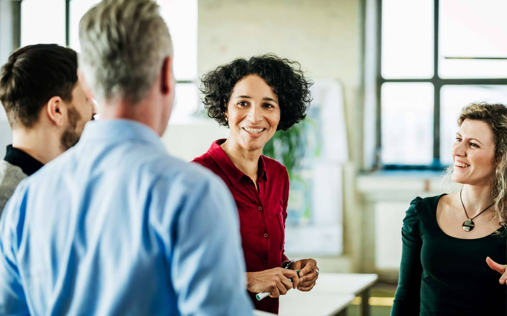 Harmoniebedürfnis: Eine Frau diskutiert lächelnd mit mehreren Arbeitskollegen.