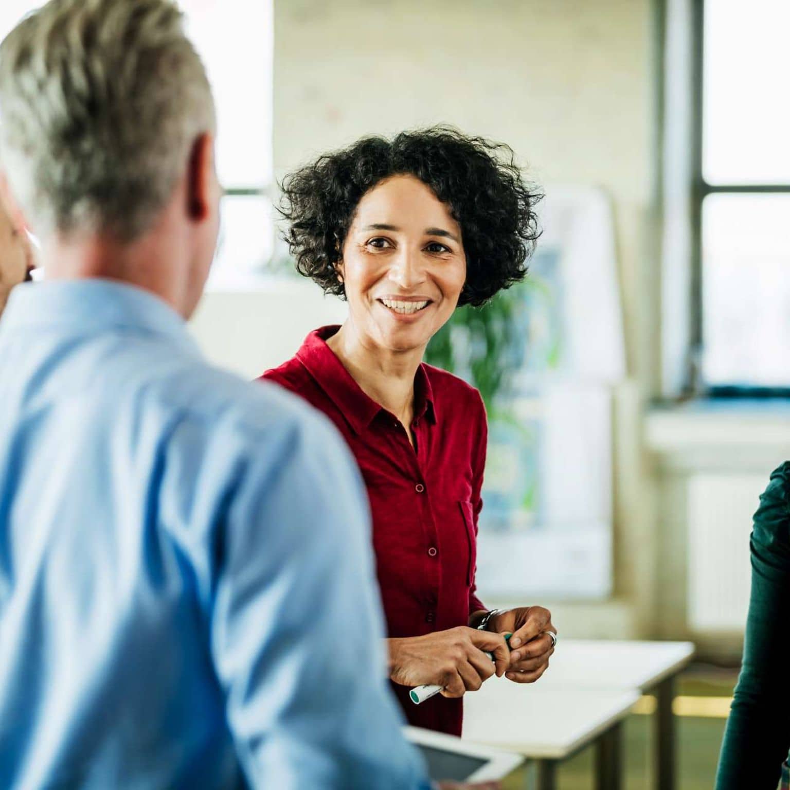 Harmoniebedürfnis: Eine Frau diskutiert lächelnd mit mehreren Arbeitskollegen.