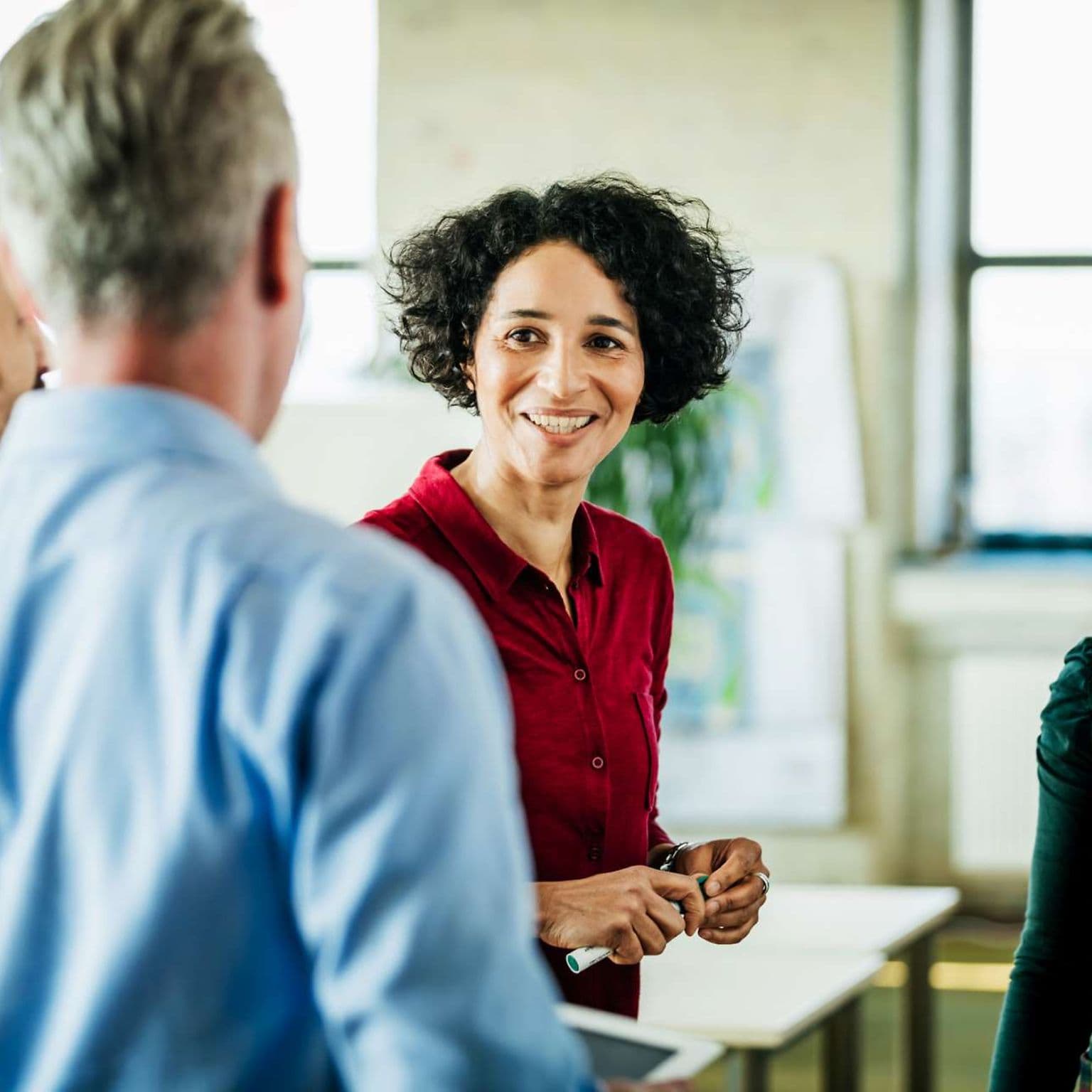 Harmoniebedürfnis: Eine Frau diskutiert lächelnd mit mehreren Arbeitskollegen.