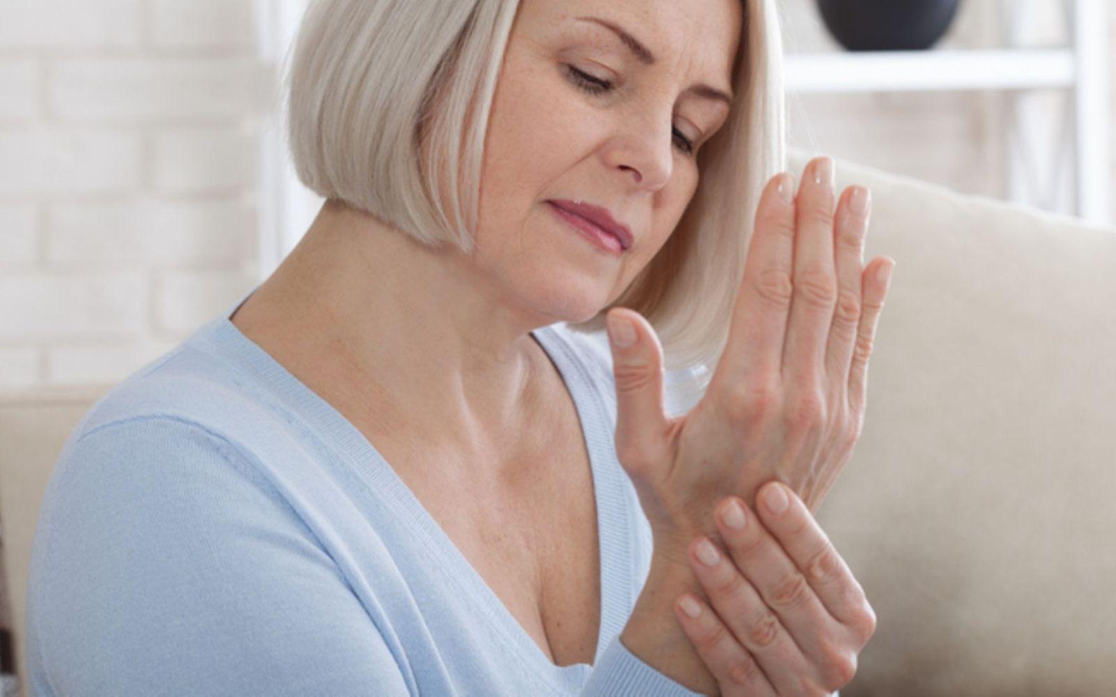 Gicht: Eine Frau mittleren Alters massiert sich ihre schmerzende Hand