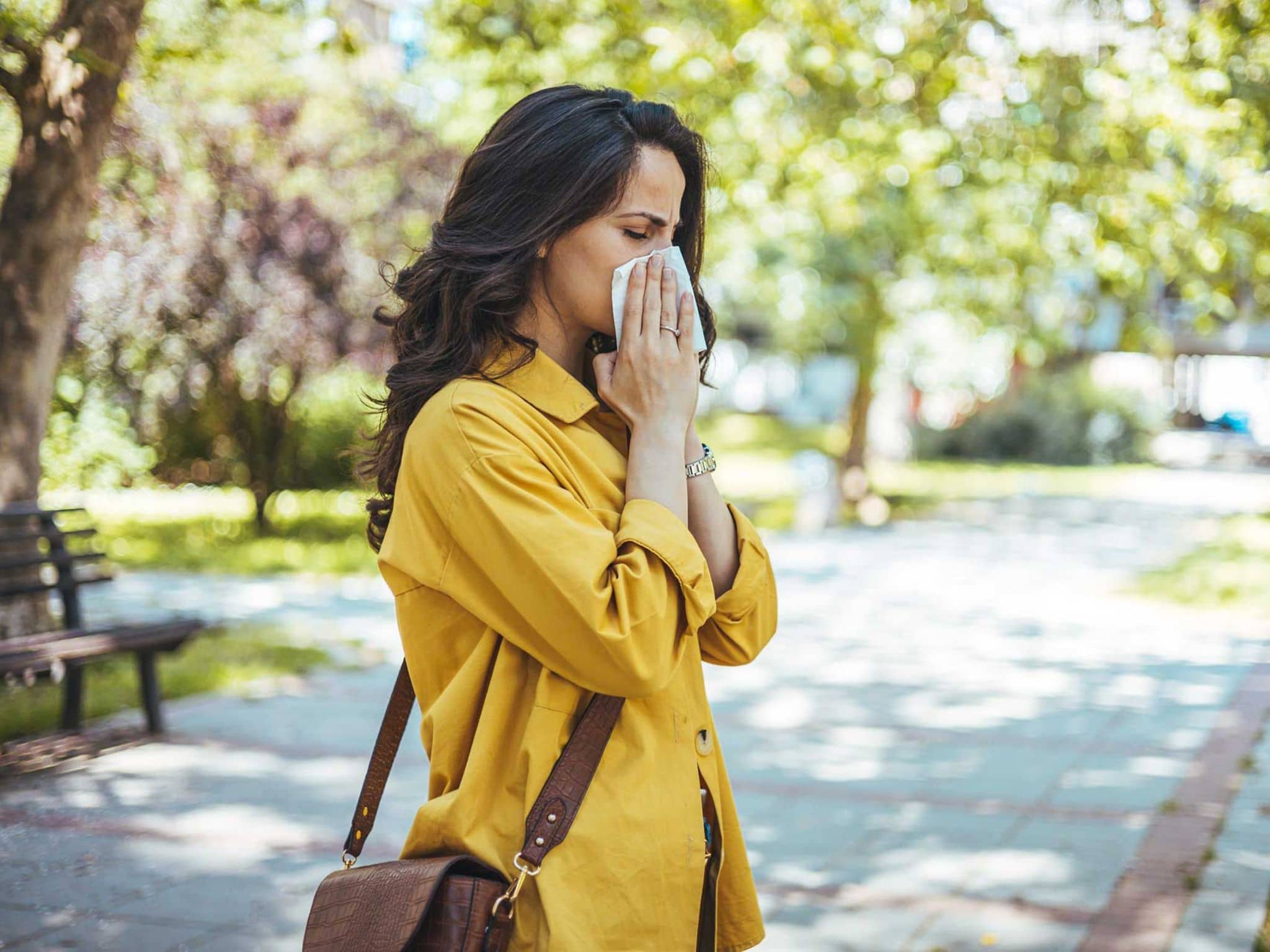 Frau im sommerlichen Outfit putzt sich die Nase im Park