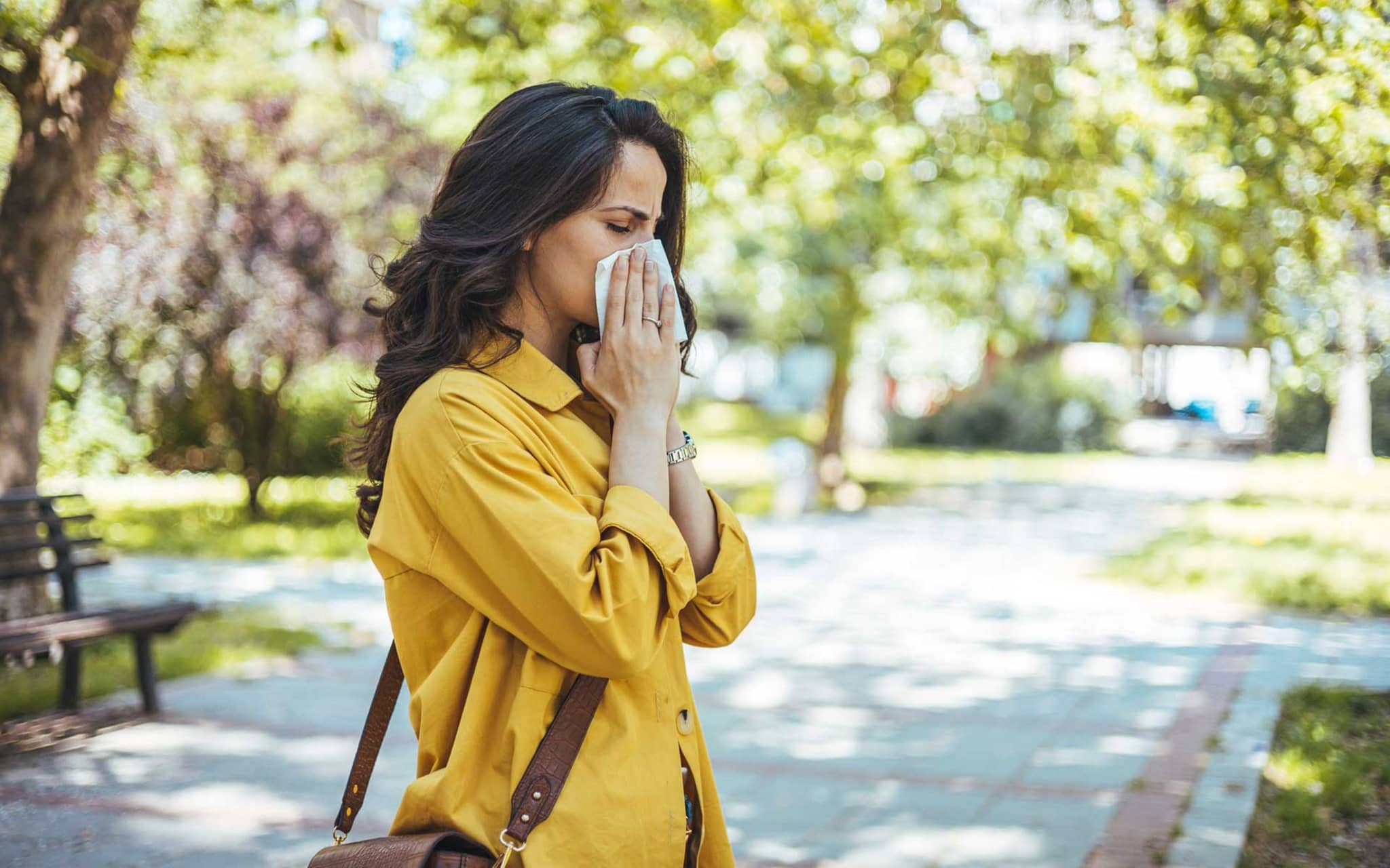 Frau im sommerlichen Outfit putzt sich die Nase im Park