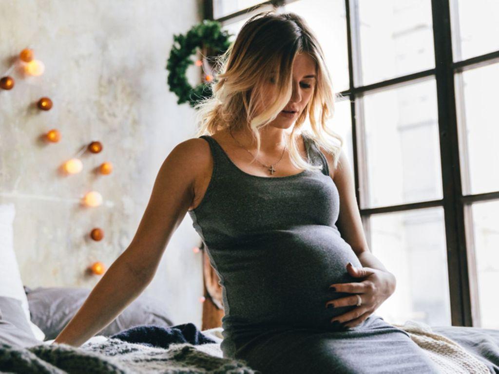 Unruhe in der Schwangerschaft: Junge Schwangere in Hauskleidung stützt sich auf dem Bett ab