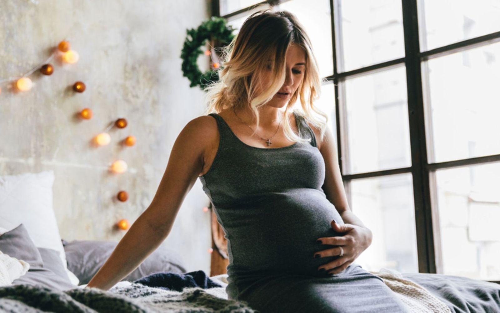 Unruhe in der Schwangerschaft: Junge Schwangere in Hauskleidung stützt sich auf dem Bett ab