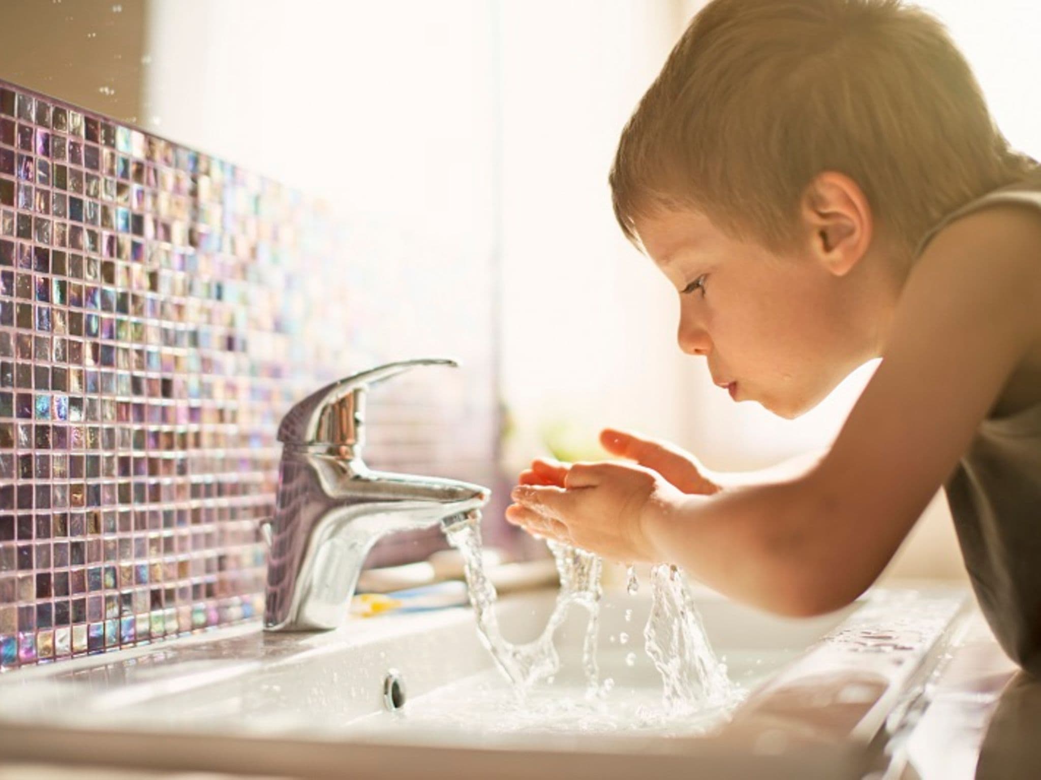Mineralwasser oder Leitungswasser: Kleiner Junge trinkt Leitungswasser im Badezimmer.