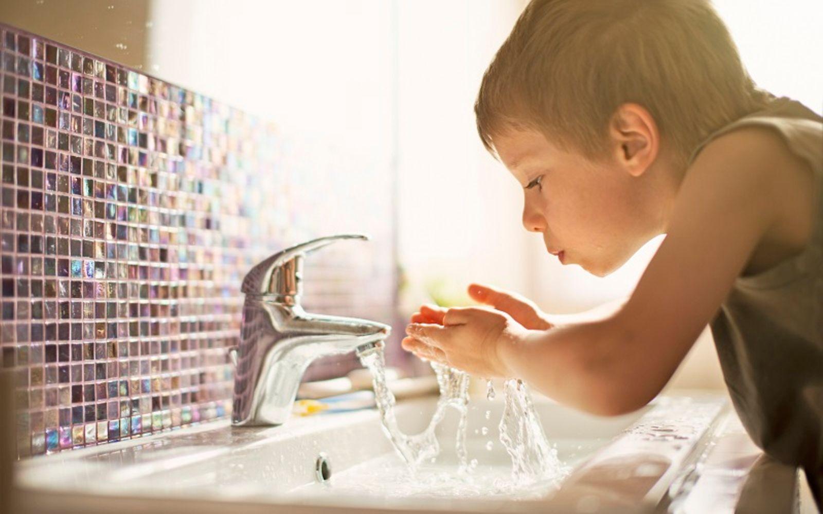 Mineralwasser oder Leitungswasser: Kleiner Junge trinkt Leitungswasser im Badezimmer.