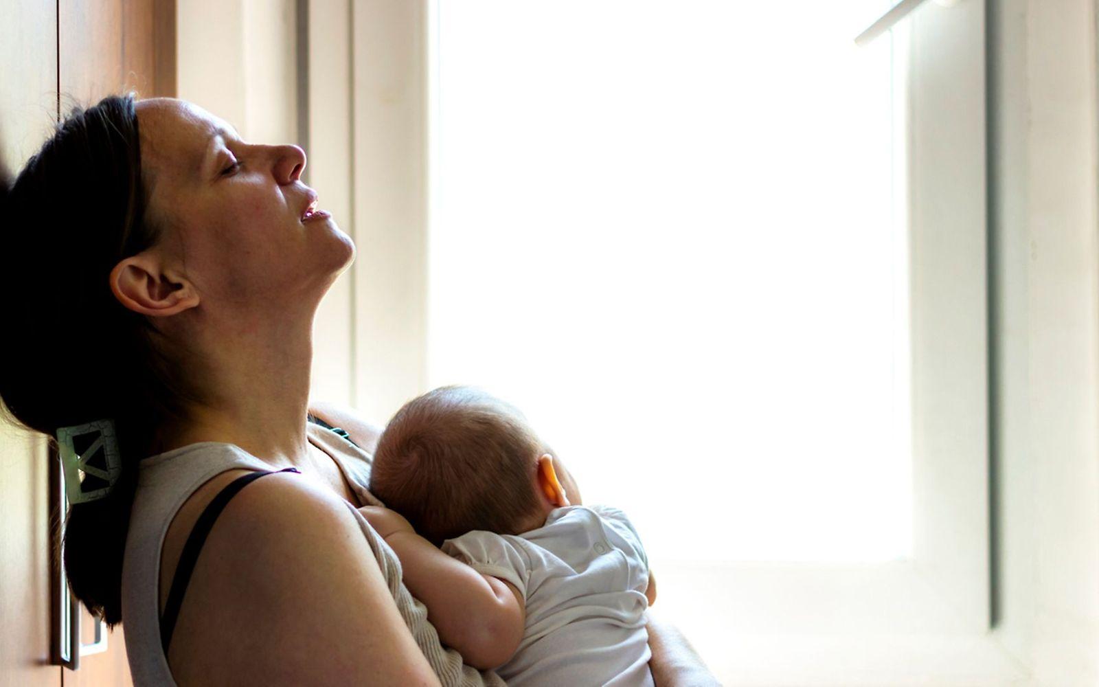 Geburtstrauma: Eine Mutter lehnt erschöpft an der Wand und hält ihr Neugeborenes