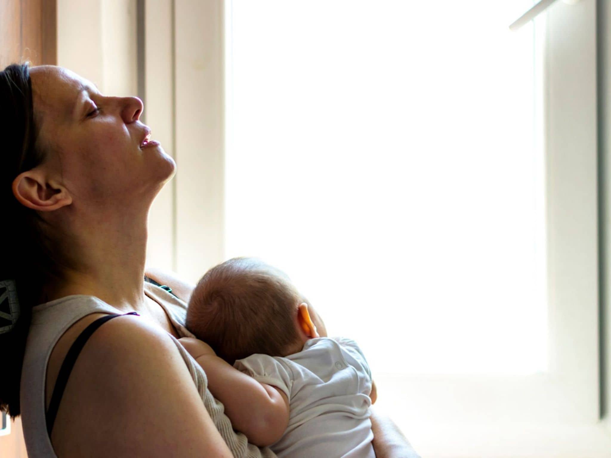 Geburtstrauma: Eine Mutter lehnt erschöpft an der Wand und hält ihr Neugeborenes