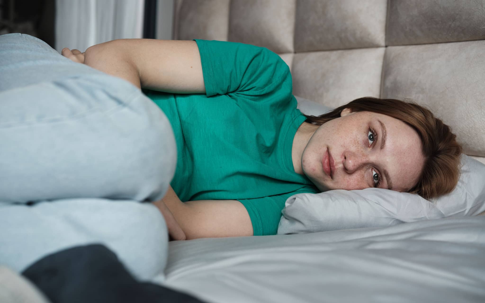 Eine Frau liegt starr im Bett und guckt traurig.